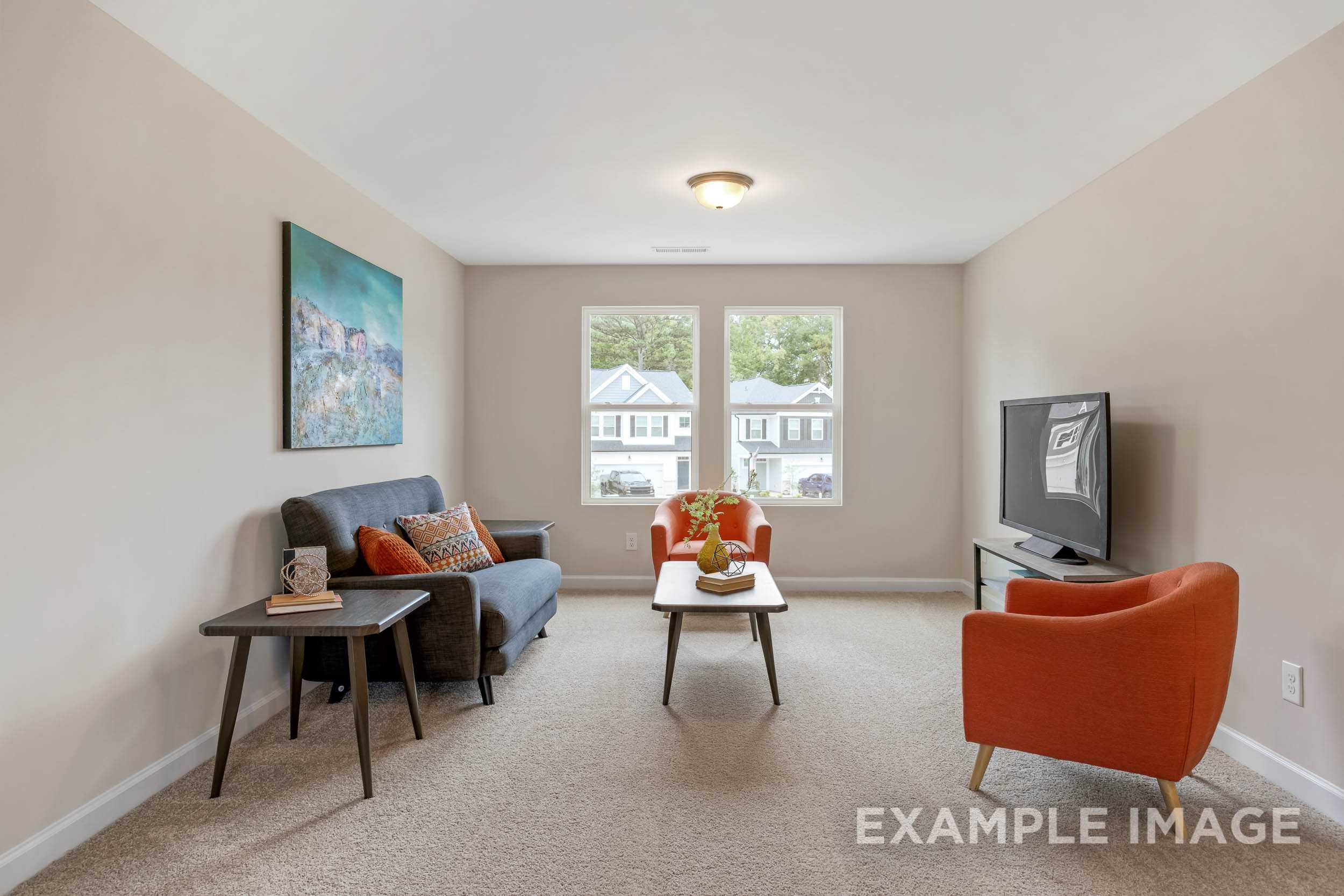 Spacious upper-floor bonus room in The Preston B with gray sofa, orange armchair, TV, and large neighborhood-view windows