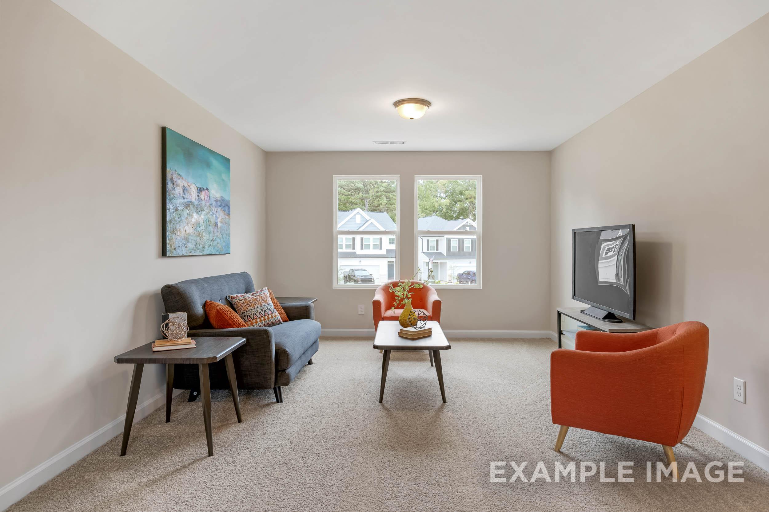 Spacious upper-floor bonus room in The Preston B with gray sofa, orange armchair, TV, and large neighborhood-view windows