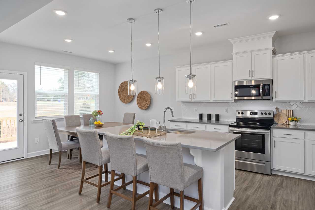 Modern open-concept kitchen at Gregory Village in Lillington NC with white shaker cabinets, quartz island, hardwood floors, and pendant lights