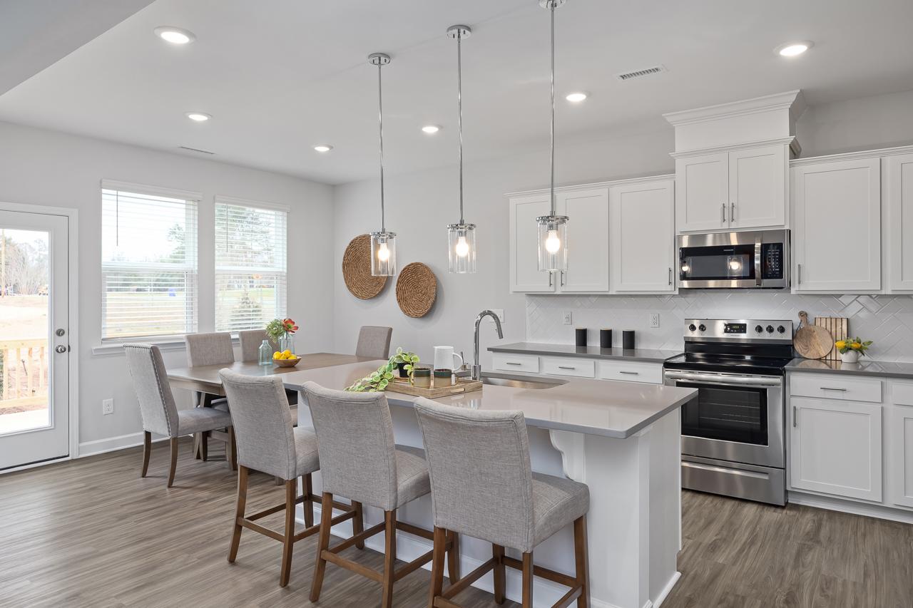 Modern open-concept kitchen at Gregory Village in Lillington NC with white shaker cabinets, quartz island, hardwood floors, and pendant lights
