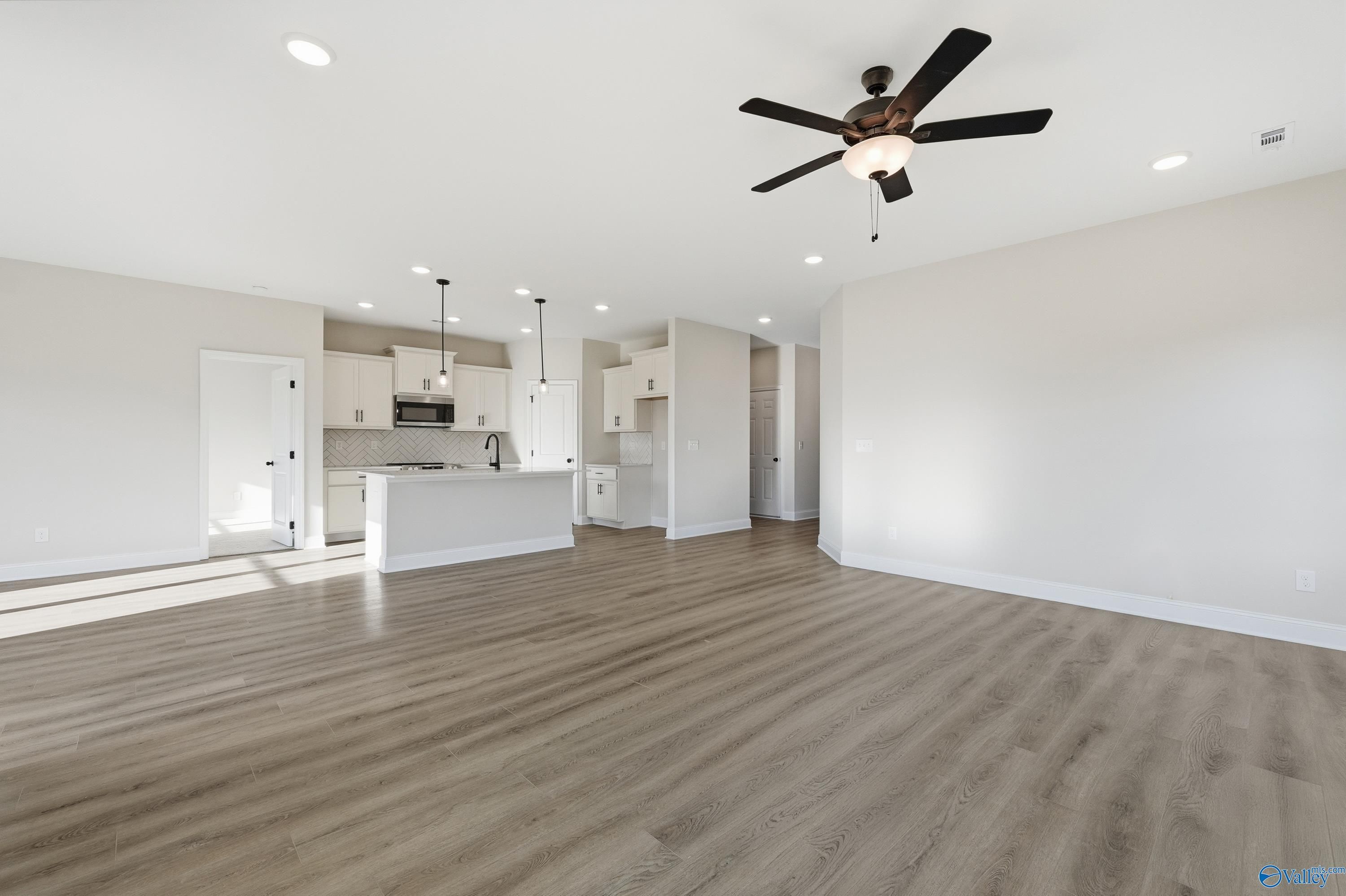 Open-concept kitchen with white cabinets, large island sink, and adjacent living area featuring light wood floors and ceiling fans in The Franklin E, Hazel Green