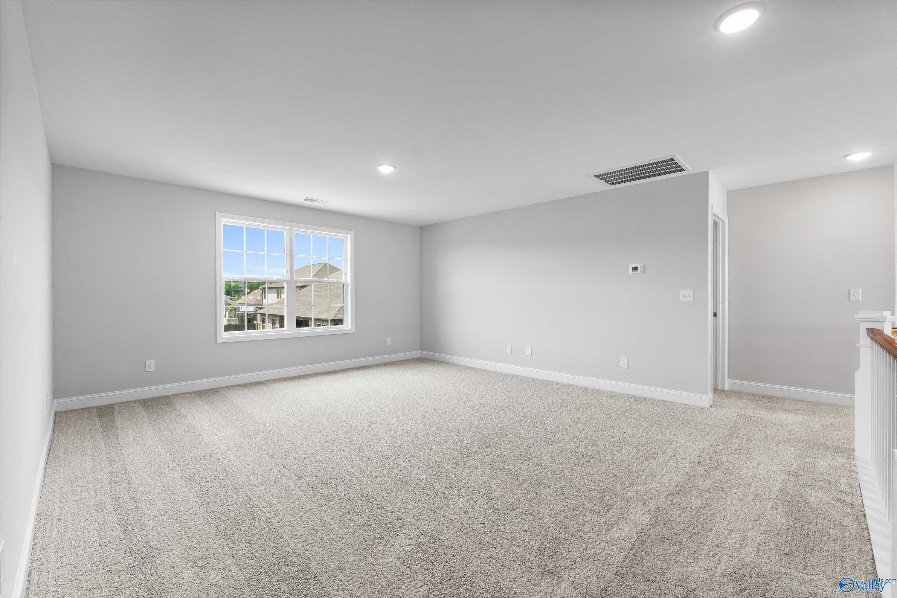 Spacious empty bedroom with large window overlooking neighborhood, neutral gray walls, carpet flooring in Davidson Homes The Madison A, Toney, Alabama