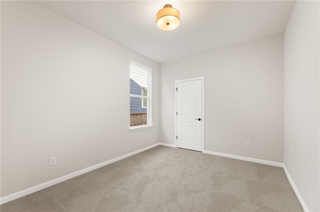 Bright secondary bedroom with neutral gray walls, beige carpet, white door, and window in Davidson Homes The Glenwood A, Loganville, GA