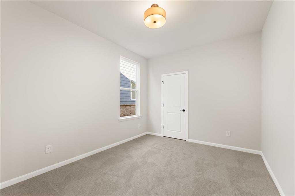 Bright secondary bedroom with light gray walls, beige carpet, window blinds, and white door in Davidson Homes The Glenwood A, Loganville, GA
