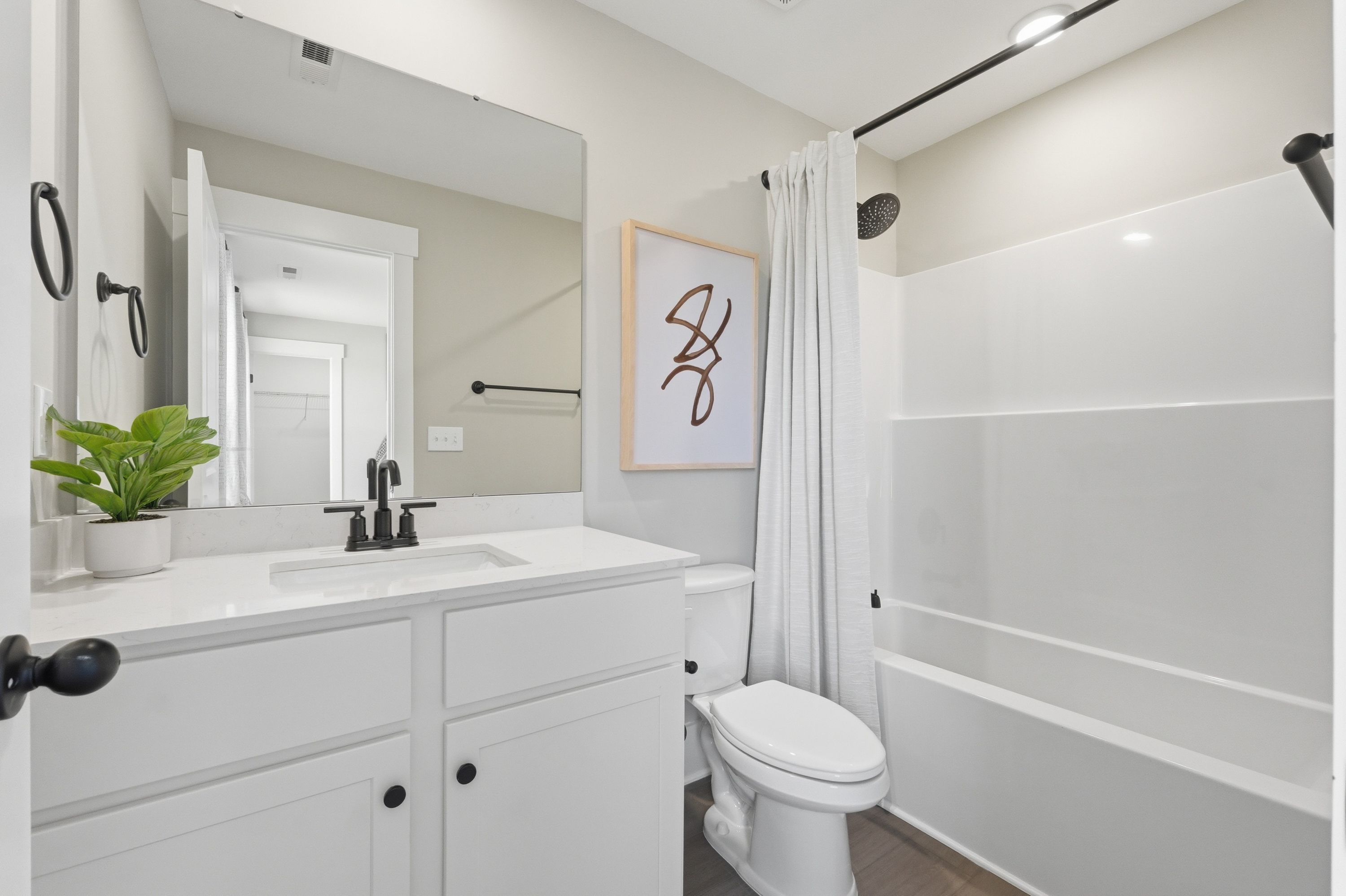 Modern bathroom at Berry Cove in New Market, Alabama with white vanity, soaking tub, abstract wall art, and potted plant