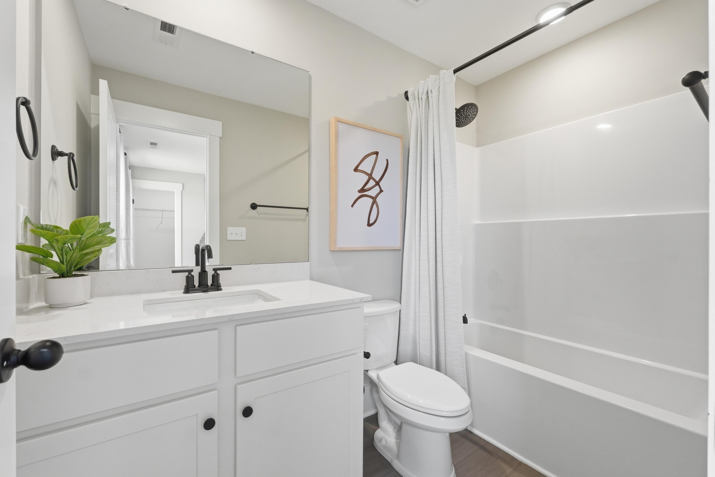 Modern bathroom at Berry Cove in New Market, Alabama with white vanity, soaking tub, abstract wall art, and potted plant