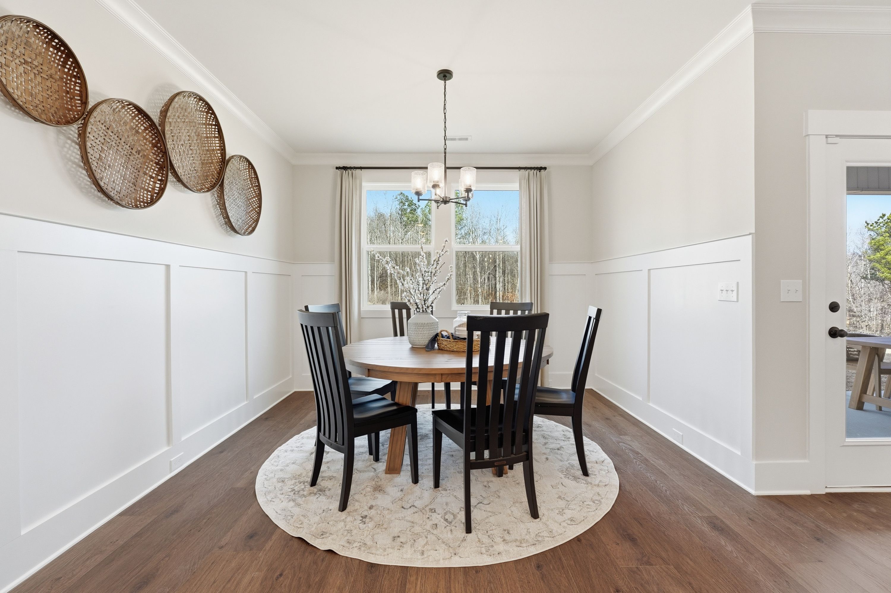 Spacious dining room in Noble Ridge Cullman Alabama with round wooden table black chairs chandelier shiplap walls and woven wall baskets