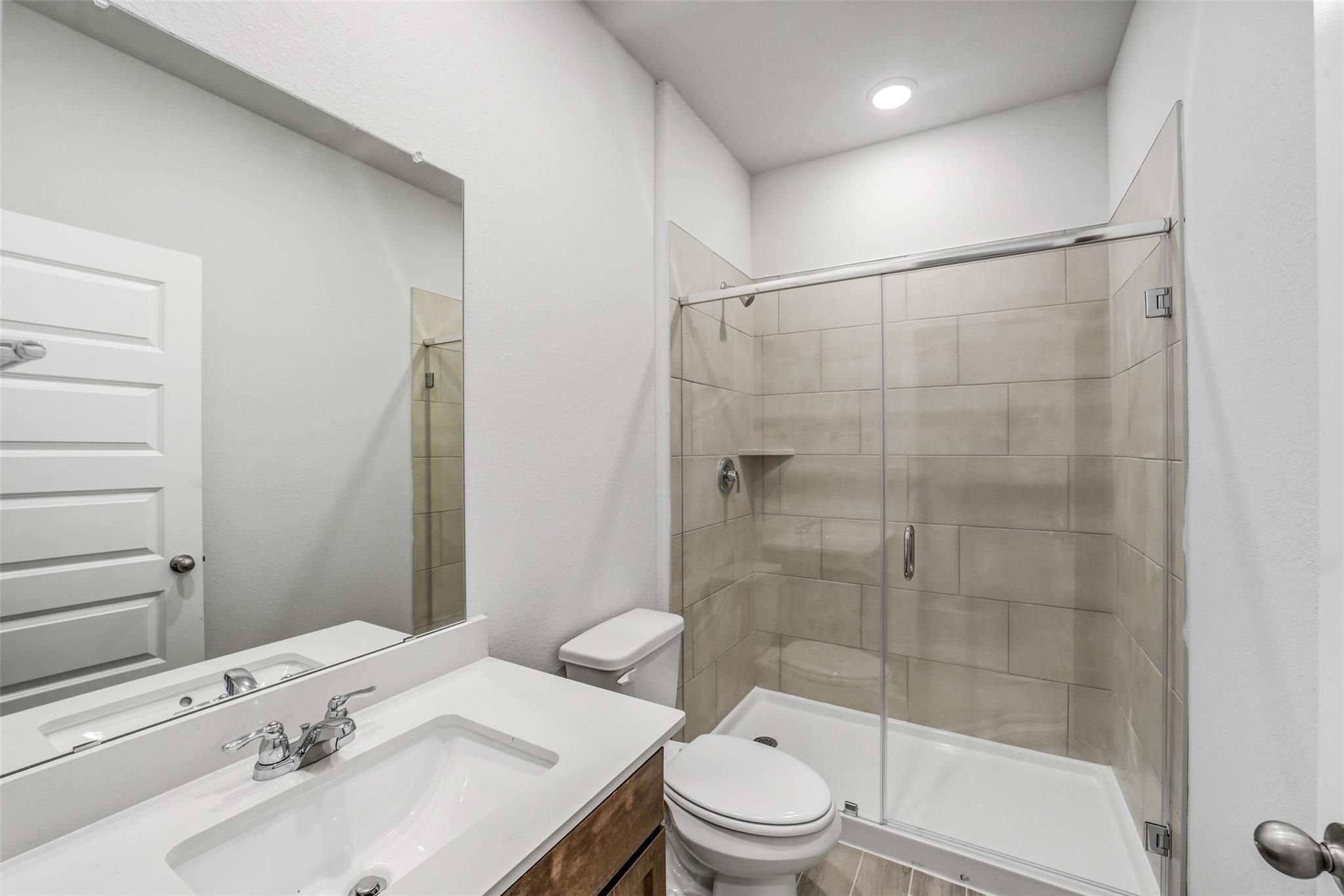 Modern bathroom with white quartz vanity, chrome faucet, glass shower enclosure, and beige subway tiles in Davidson Homes The Acadia C, Magnolia Texas