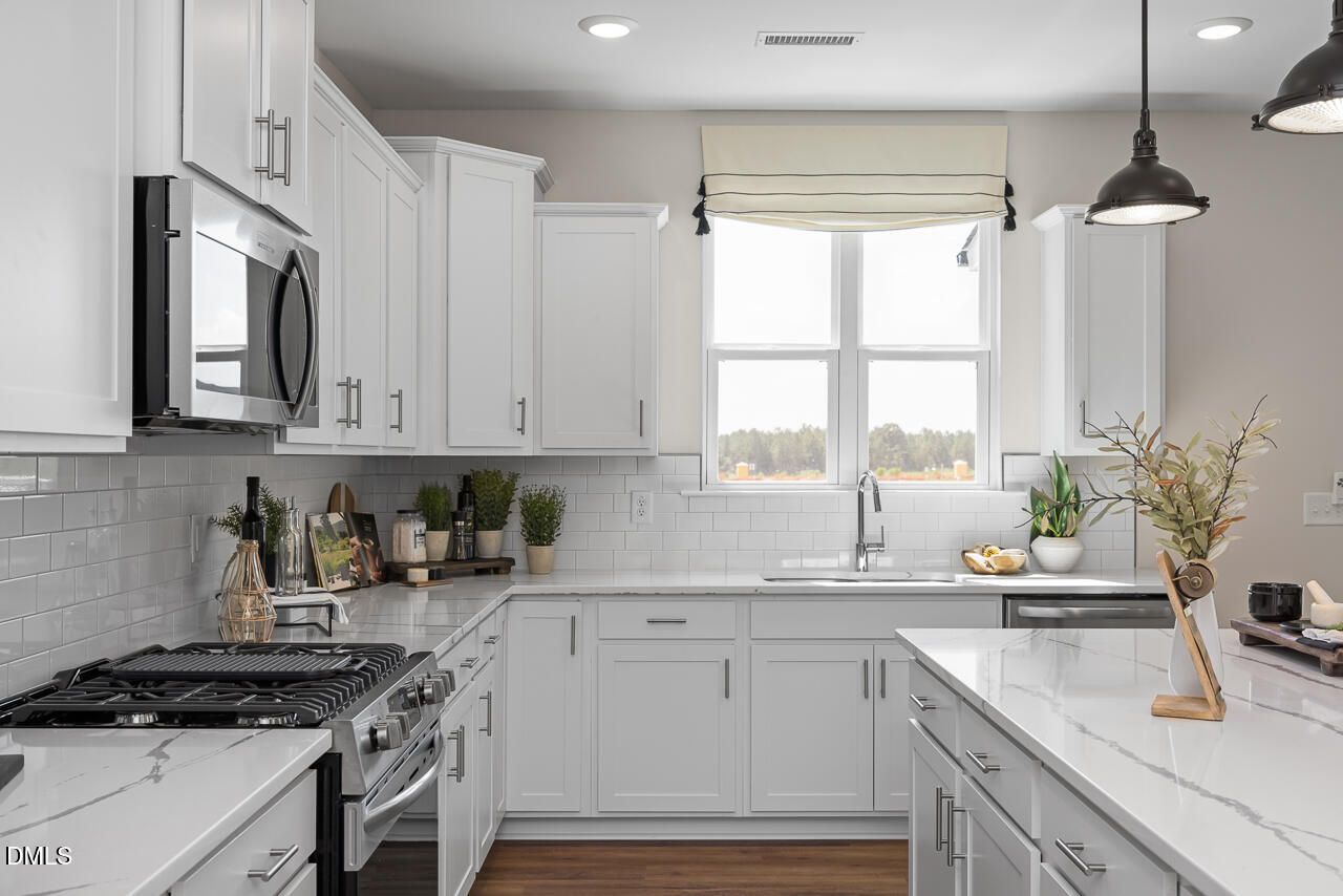 Modern white kitchen with quartz island, subway tile backsplash, stainless appliances in Davidson Homes Hickory II B, Zebulon NC