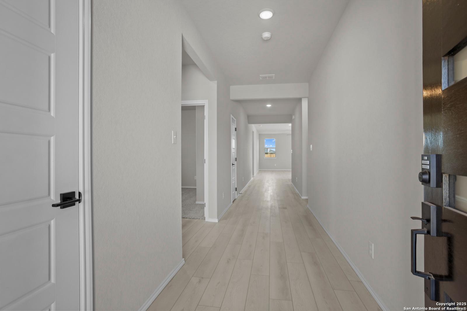 Long hallway with light oak floors, white walls, and window view in Davidson Homes The Daphne H, Seguin, Texas
