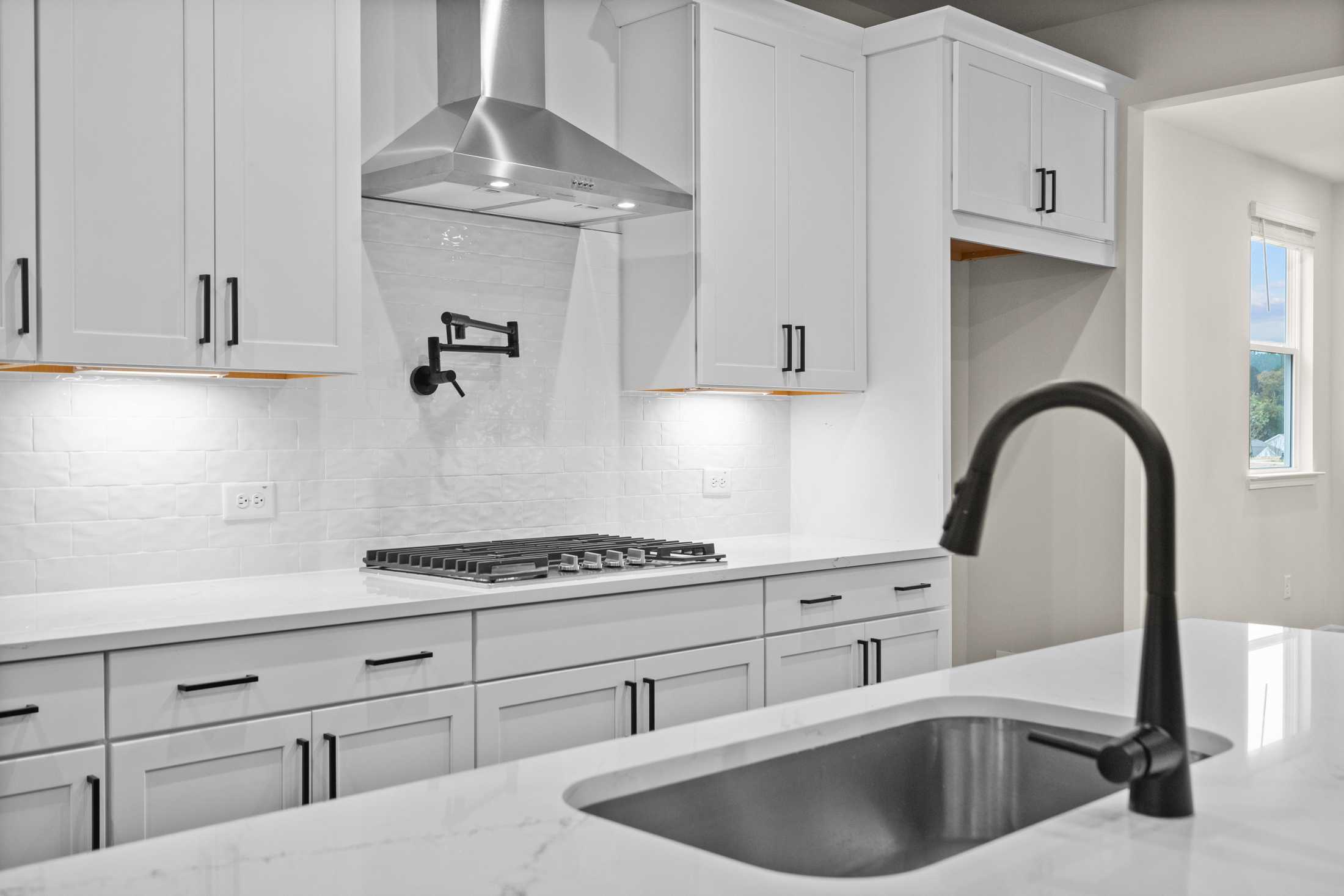 Spacious modern kitchen in The Glenwood B featuring white shaker cabinets, gas cooktop, black faucet, and quartz island