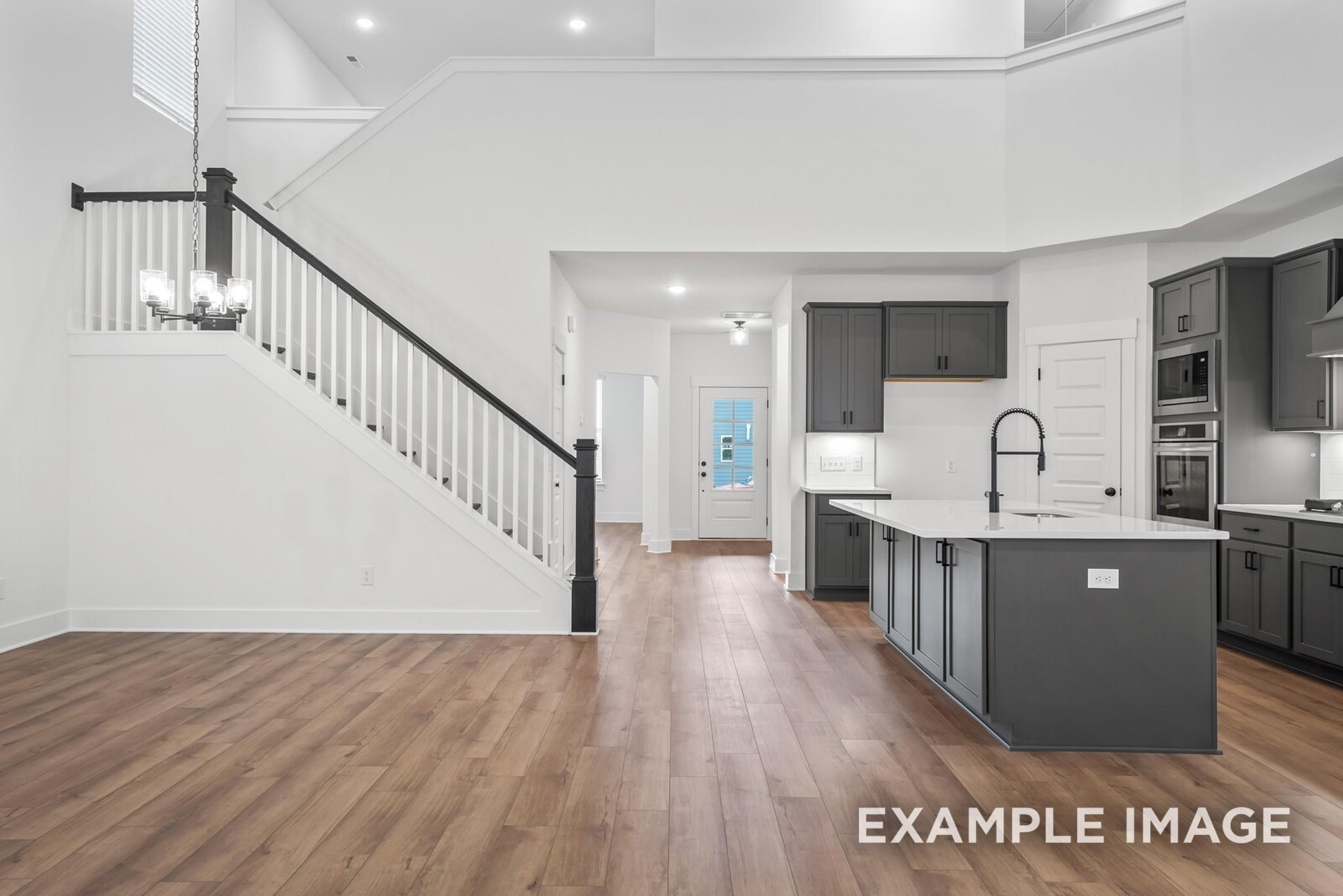 Open-concept foyer with grand white staircase and modern kitchen island, gray cabinets in Davidson Homes The Ridgeport C, Gallatin, TN