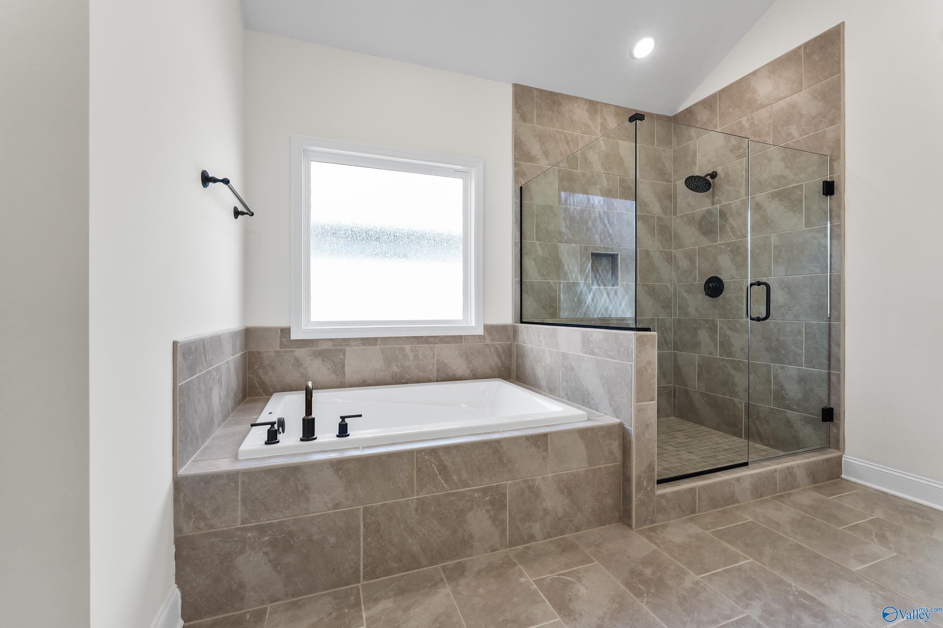Elegant master bathroom with freestanding tub, frameless glass shower, and beige tile in Davidson Homes The Finleigh, Harvest, AL
