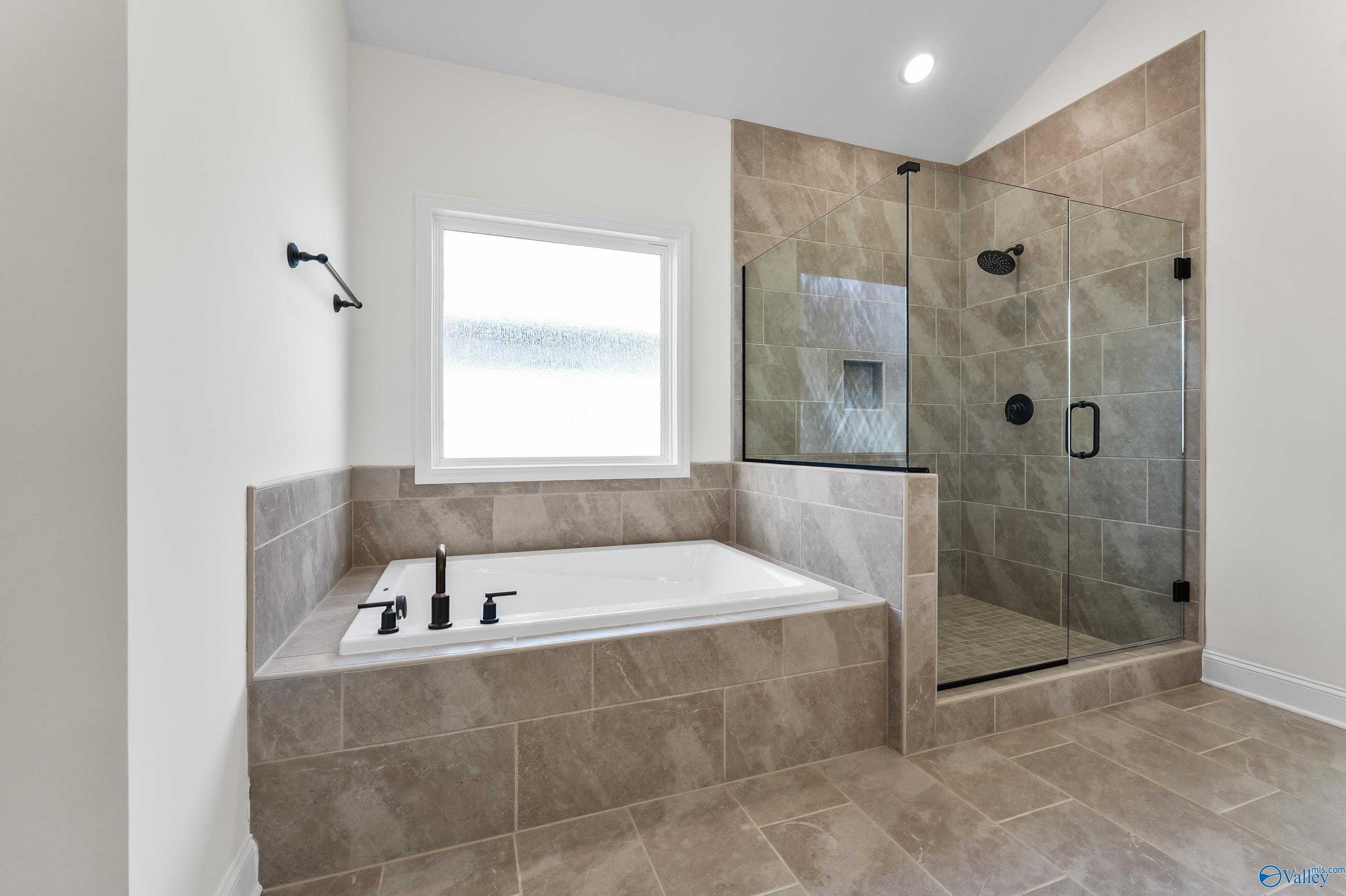 Elegant master bathroom with freestanding tub, frameless glass shower, and beige tile in Davidson Homes The Finleigh, Harvest, AL