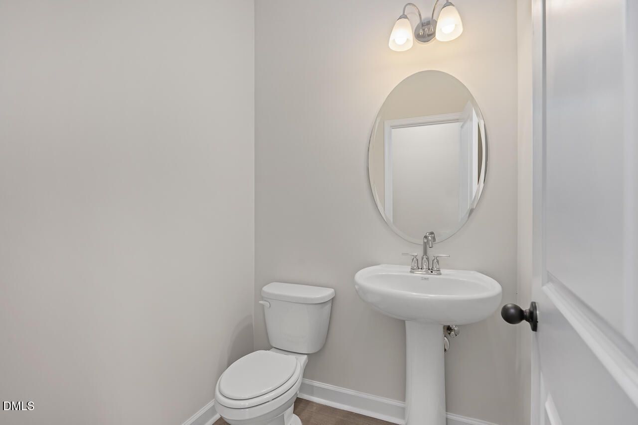 Elegant powder room with pedestal sink, round mirror, wall sconces, and white toilet in Davidson Homes The Mitchell Interior, Knightdale, NC