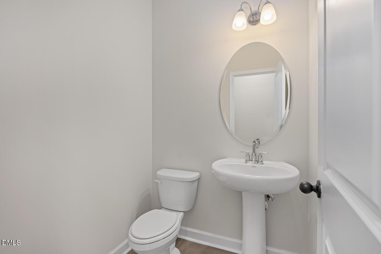 Elegant powder room with pedestal sink, round mirror, wall sconces, and white toilet in Davidson Homes The Mitchell Interior, Knightdale, NC