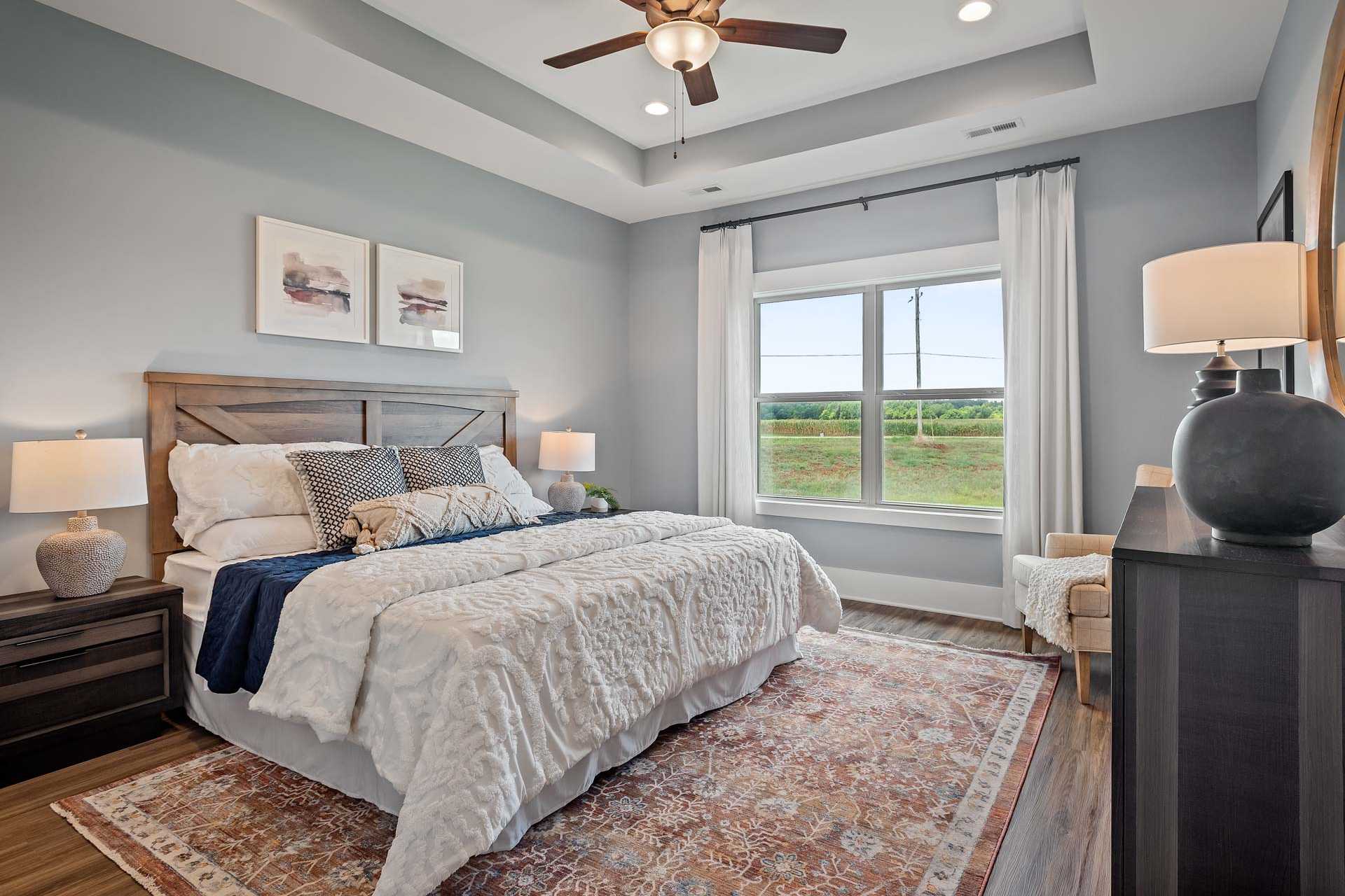 Spacious master bedroom at Heritage Lakes in New Market Alabama with gray walls king bed ceiling fan and field views