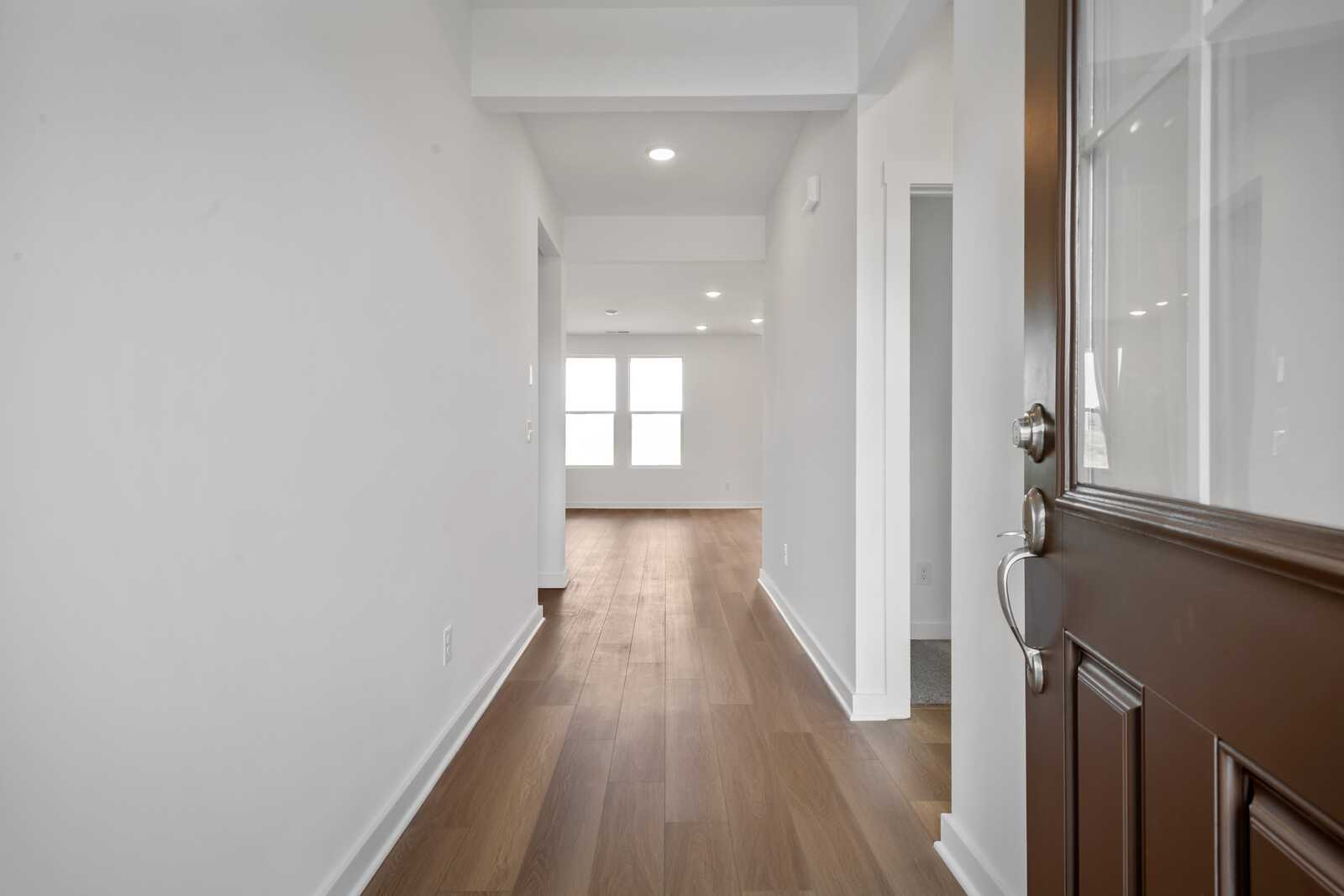 Spacious hallway in The Asheville home design with oak hardwood floors, white walls, and glass-paneled front door