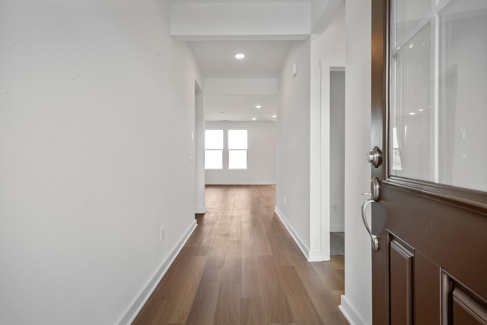 Bright hallway in The Asheville home design featuring hardwood floors, white walls, and double windows
