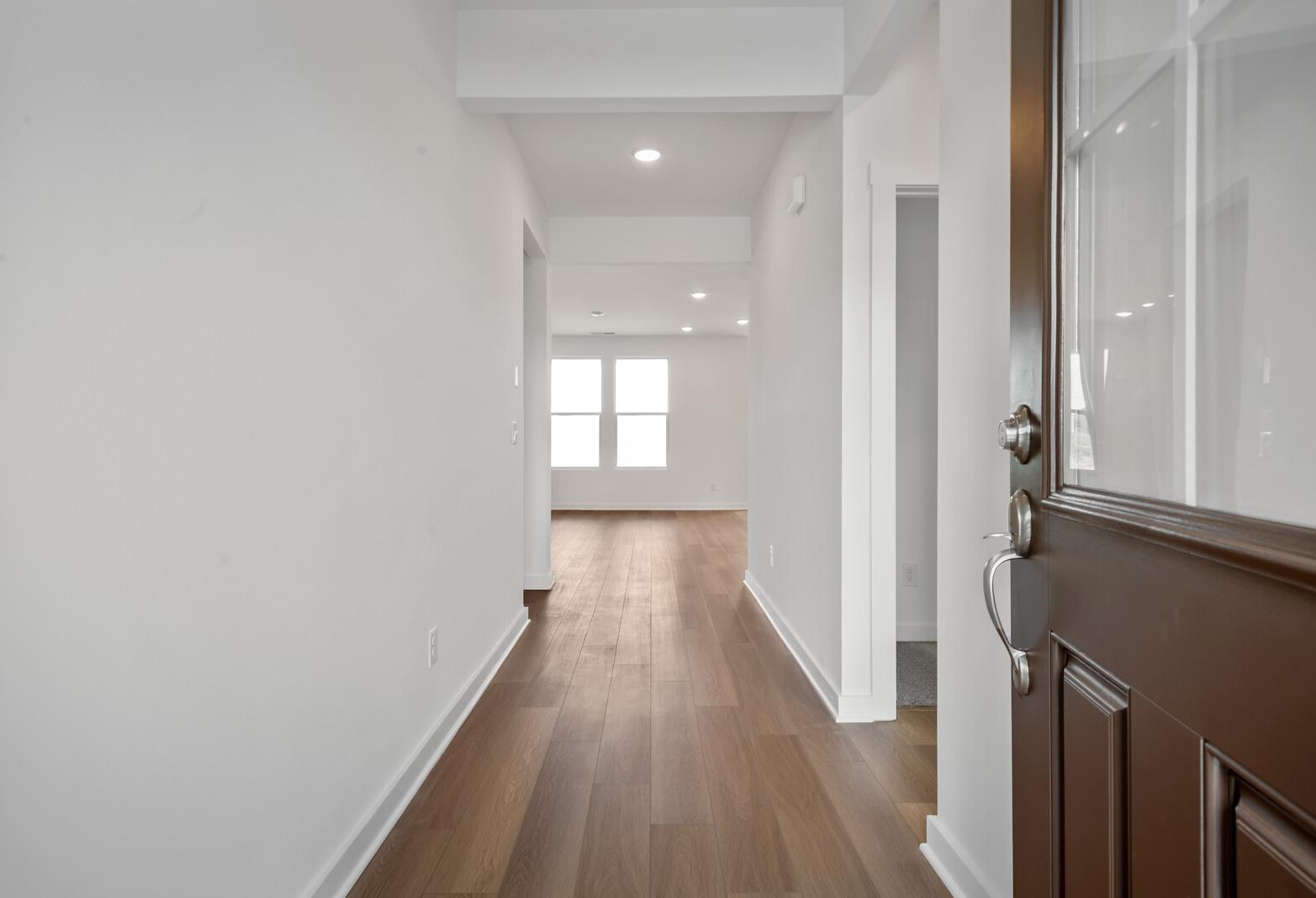 Bright hallway in The Asheville home design featuring hardwood floors, white walls, and double windows