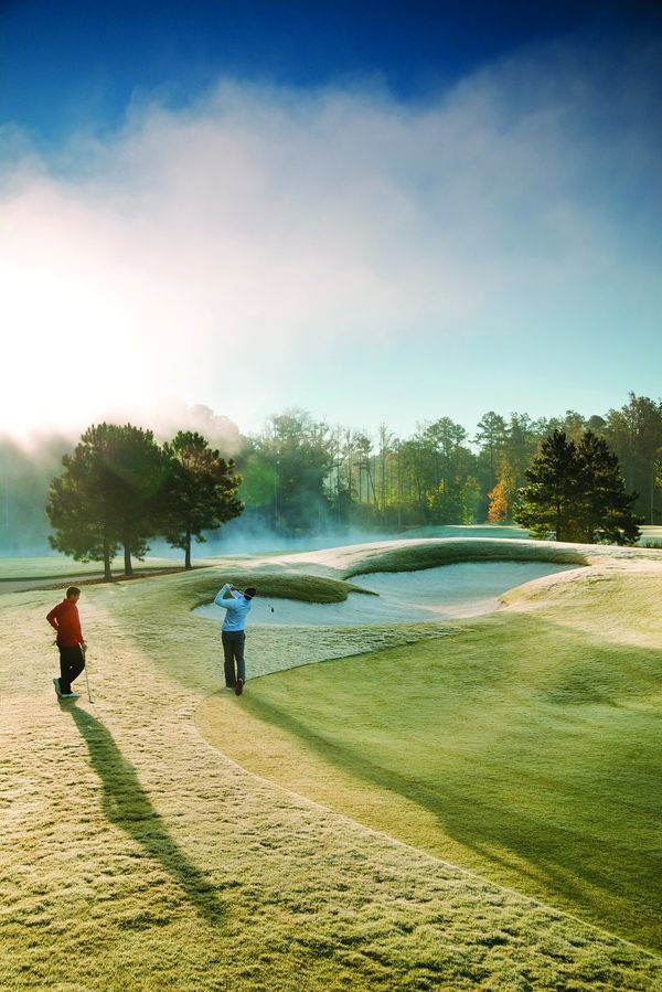Golfer swinging near sand bunker on misty morning golf course at Addison West in Holly Springs, North Carolina