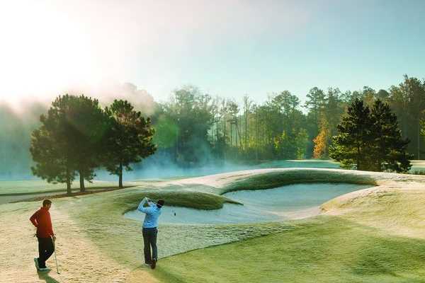 Golfer swinging near sand bunker on misty morning golf course at Addison West in Holly Springs, North Carolina