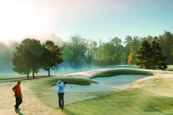 Golfer swinging near sand bunker on misty morning golf course at Addison West in Holly Springs, North Carolina