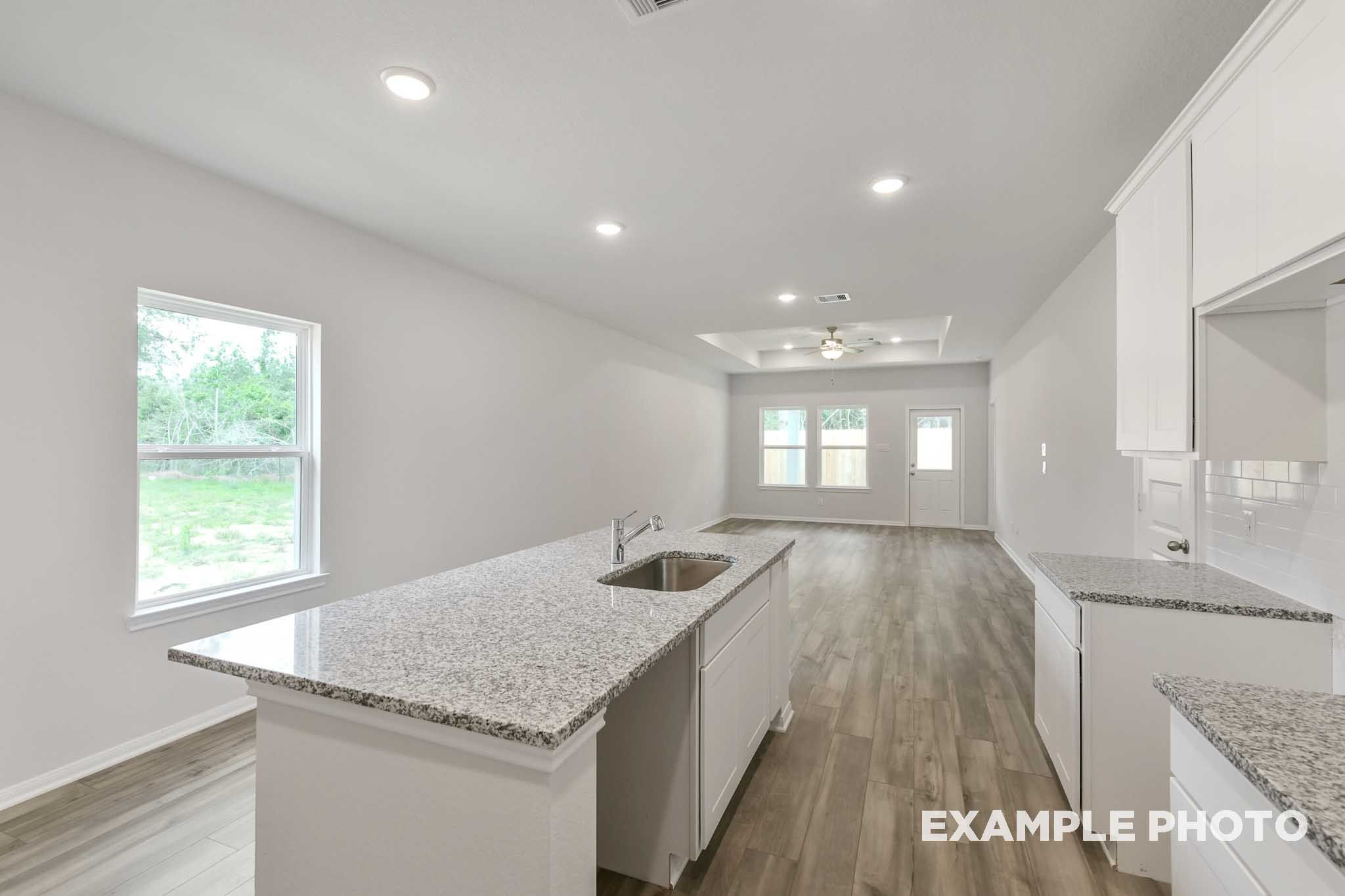 Open-concept kitchen and living area in The Frio featuring a granite island, white cabinetry, and wood-look flooring.
