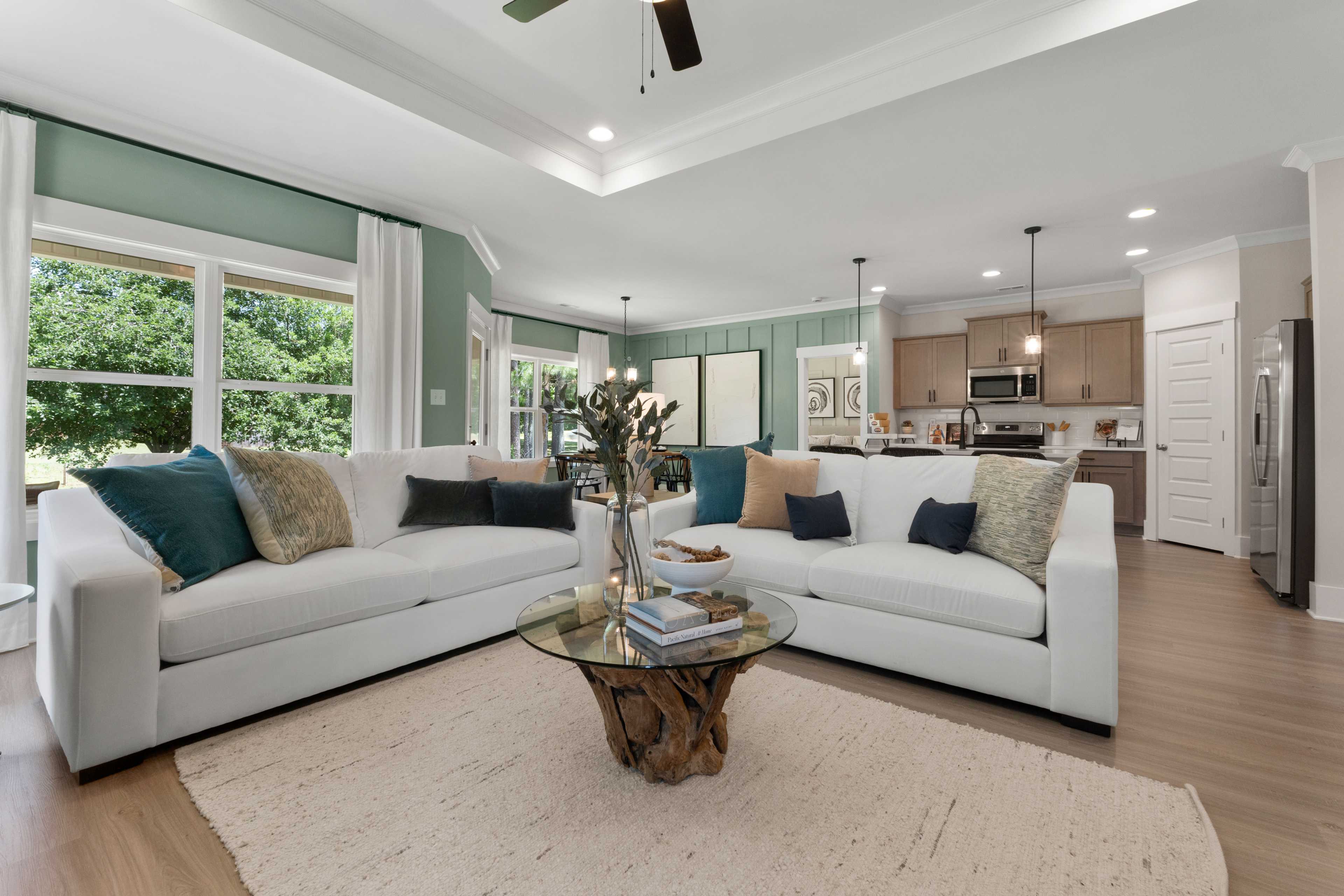 Spacious open-concept living room at Hollon Meadow in Decatur AL with white sofas, teal pillows, glass coffee table, hardwood floors, and kitchen view