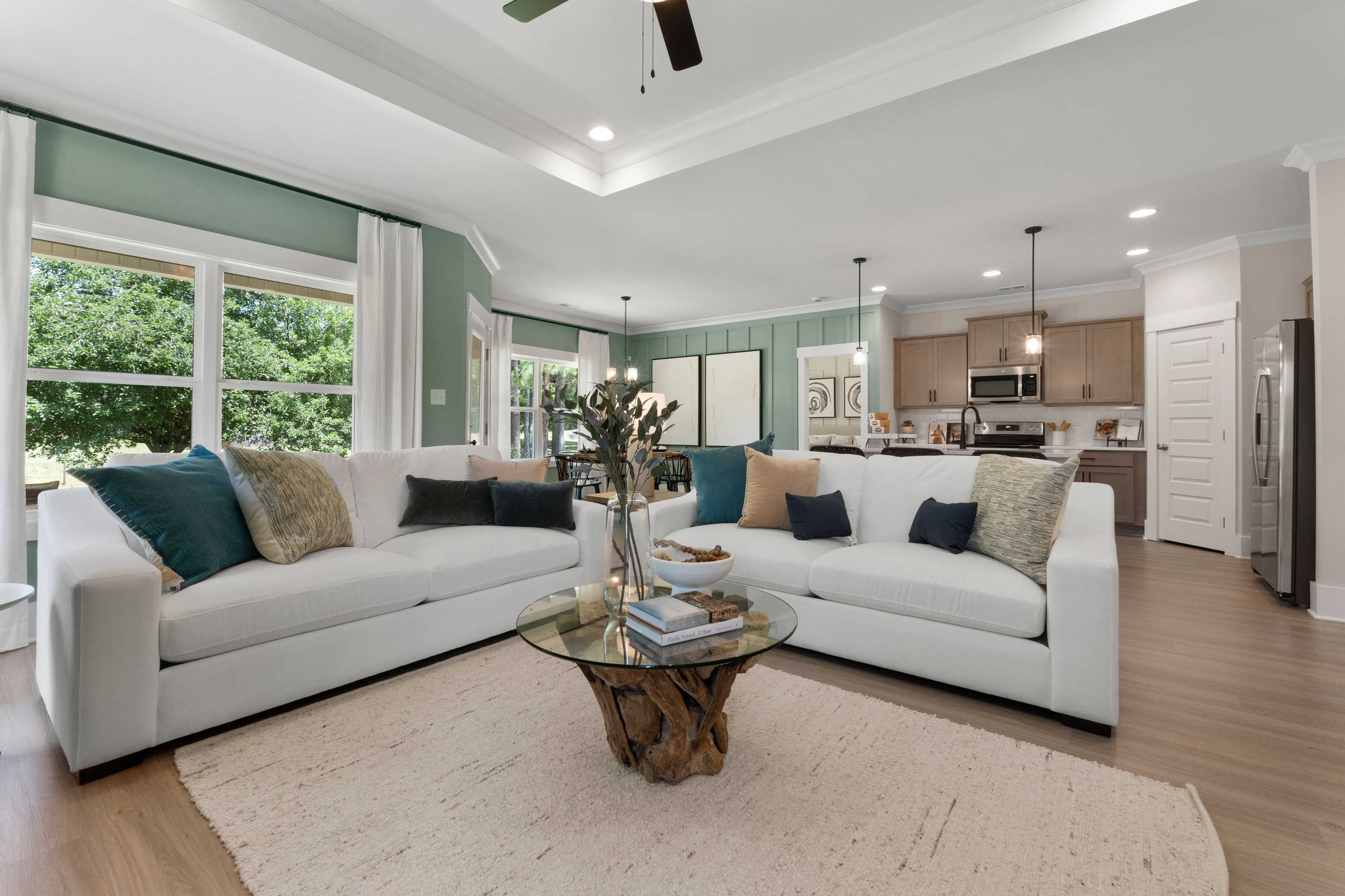 Spacious open-concept living room at Hollon Meadow in Decatur AL with white sofas, teal pillows, glass coffee table, hardwood floors, and kitchen view