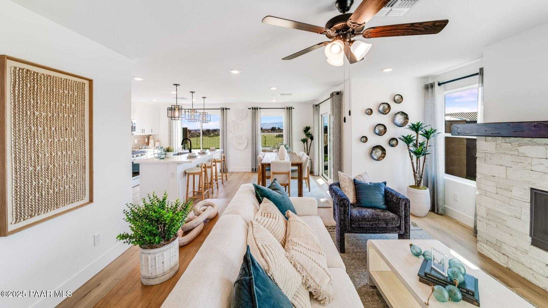 Open-concept living room with white sofa, stone fireplace, kitchen island, and large windows in Davidson Homes Wilmington B, Prescott, Arizona