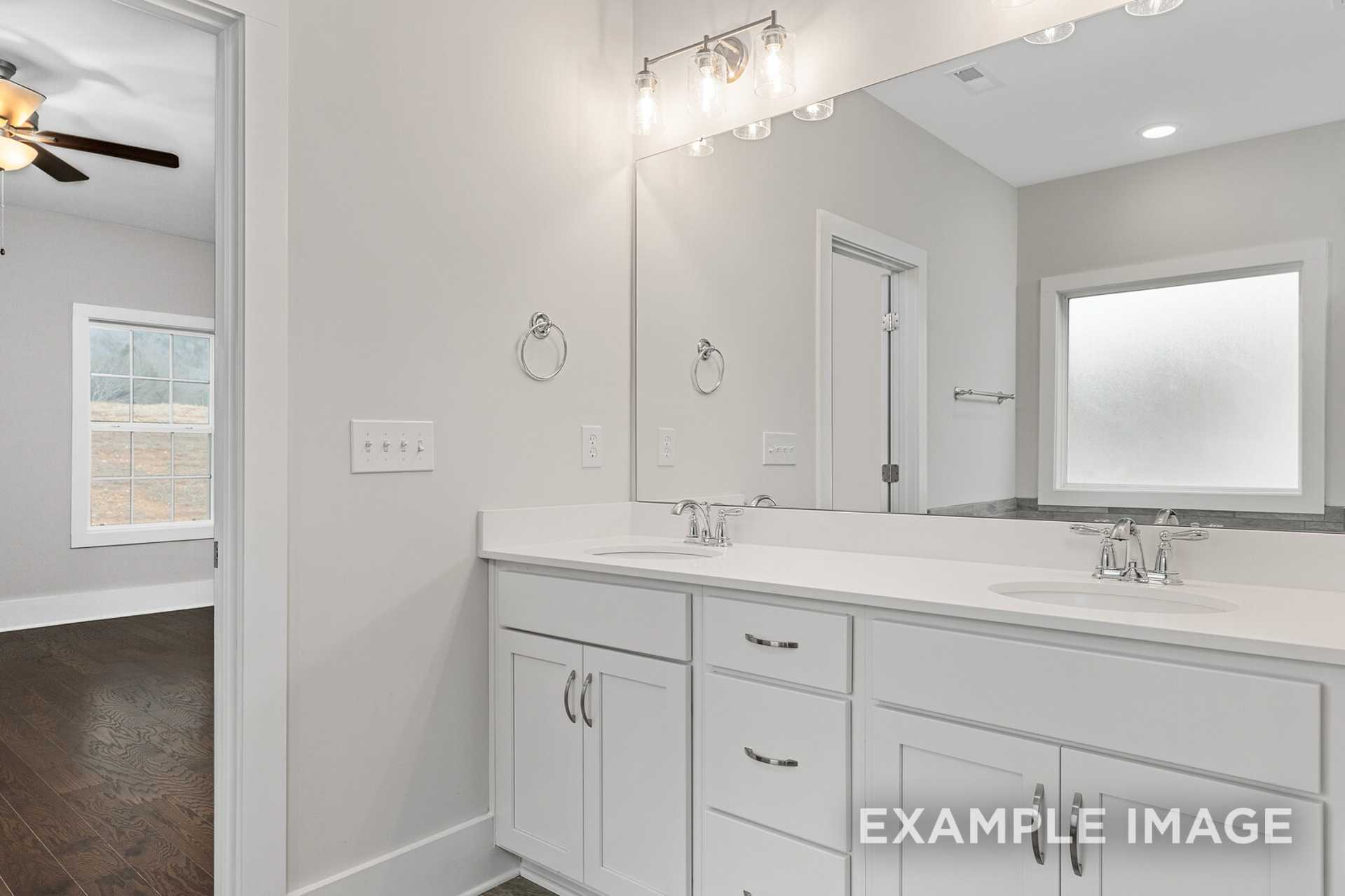 Spacious master bathroom in The Rockford with white double vanity, large mirror, frosted window, and hardwood floors