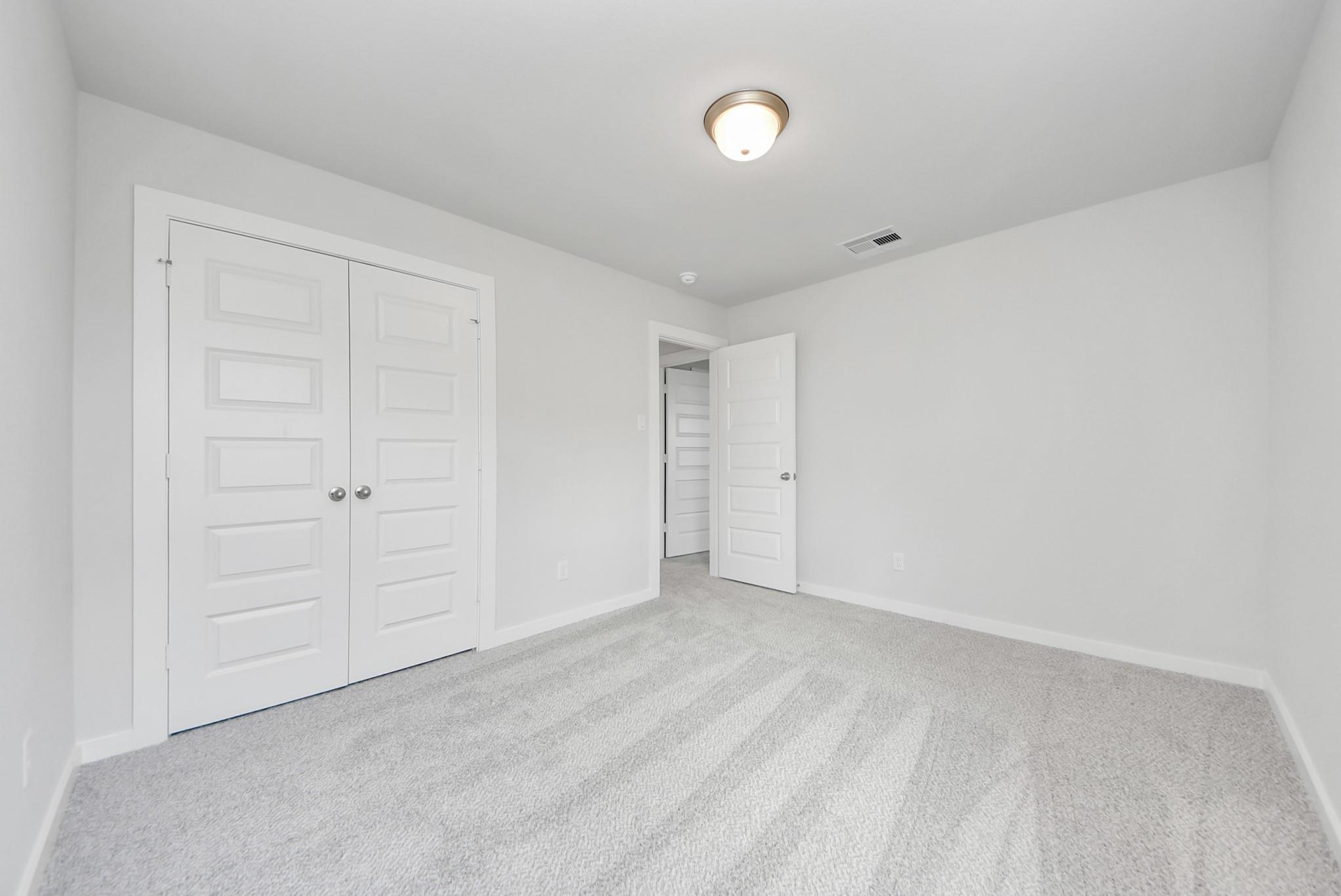 Bright secondary bedroom with carpet flooring and walk-in closet in The Verano B floor plan by Davidson Homes in Katy, TX.