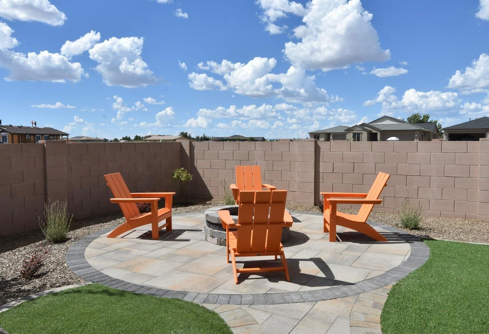 Cozy fire pit patio in The Harmony home with orange Adirondack chairs, stone pavers, and desert landscaping