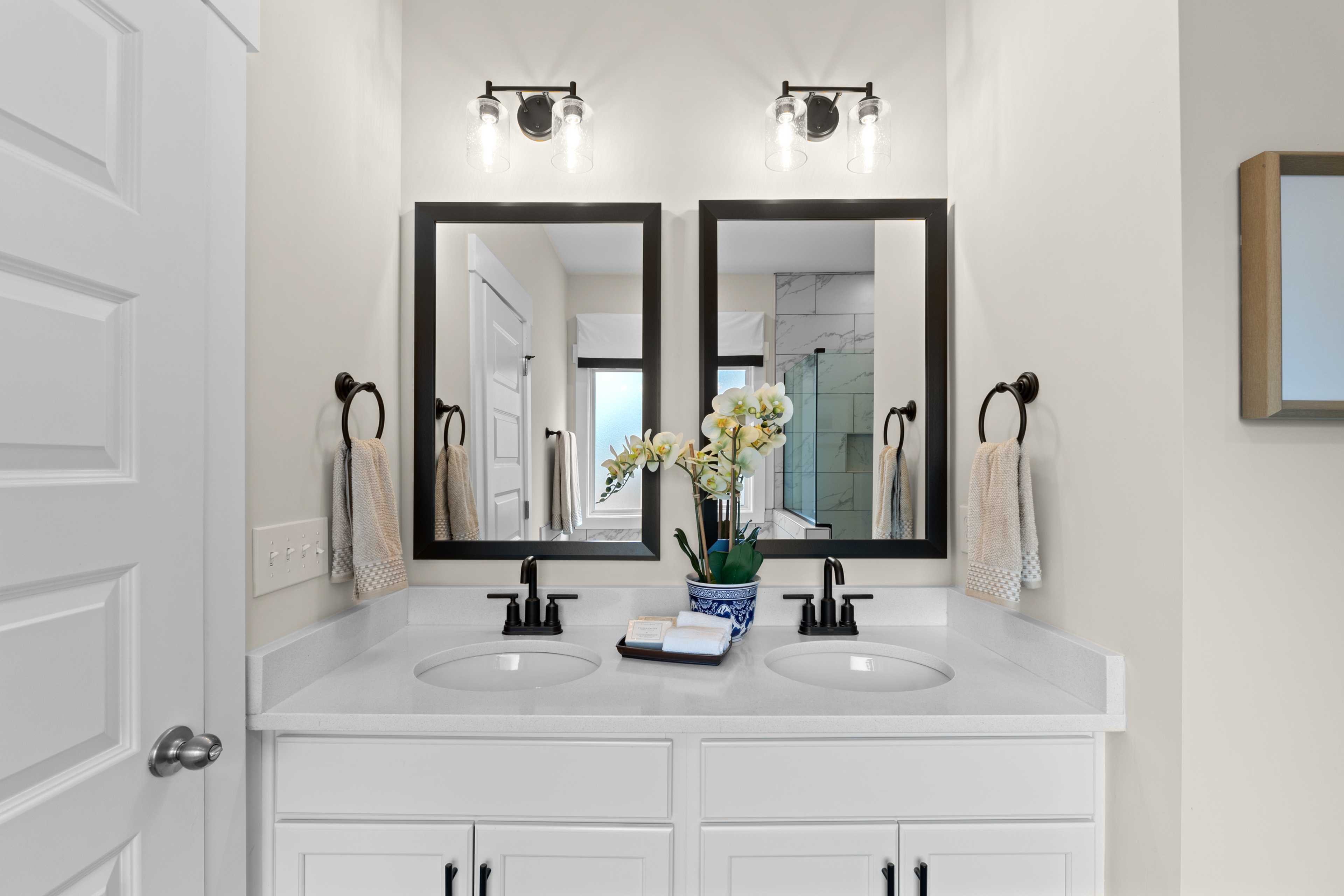 Luxury double vanity bathroom at Ivy Hills in Toney Alabama with white cabinets black mirrors and floral vase