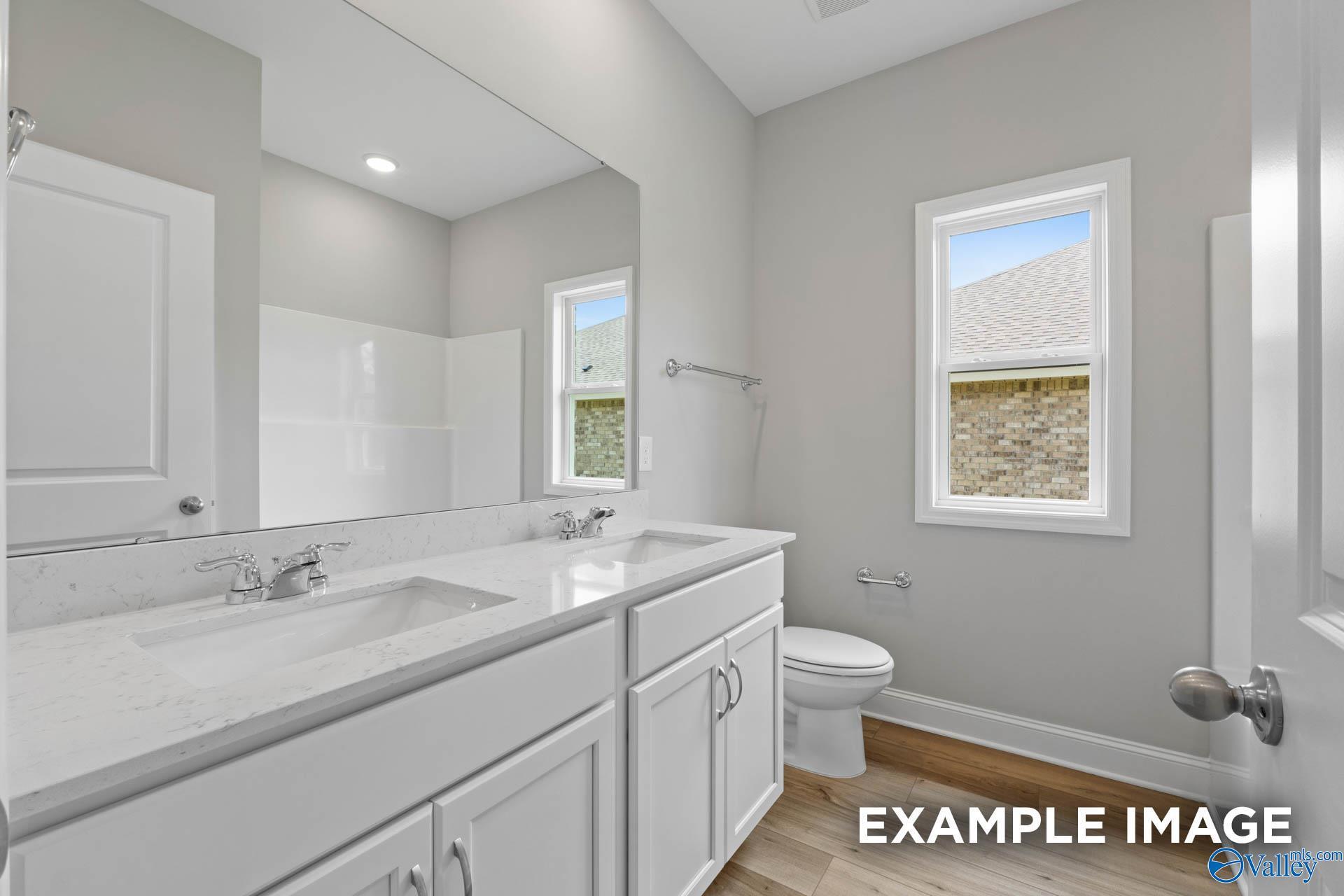 Modern master bathroom featuring double white vanity, quartz countertop, large mirror, and window in Davidson Homes The Everett B, Athens, Alabama