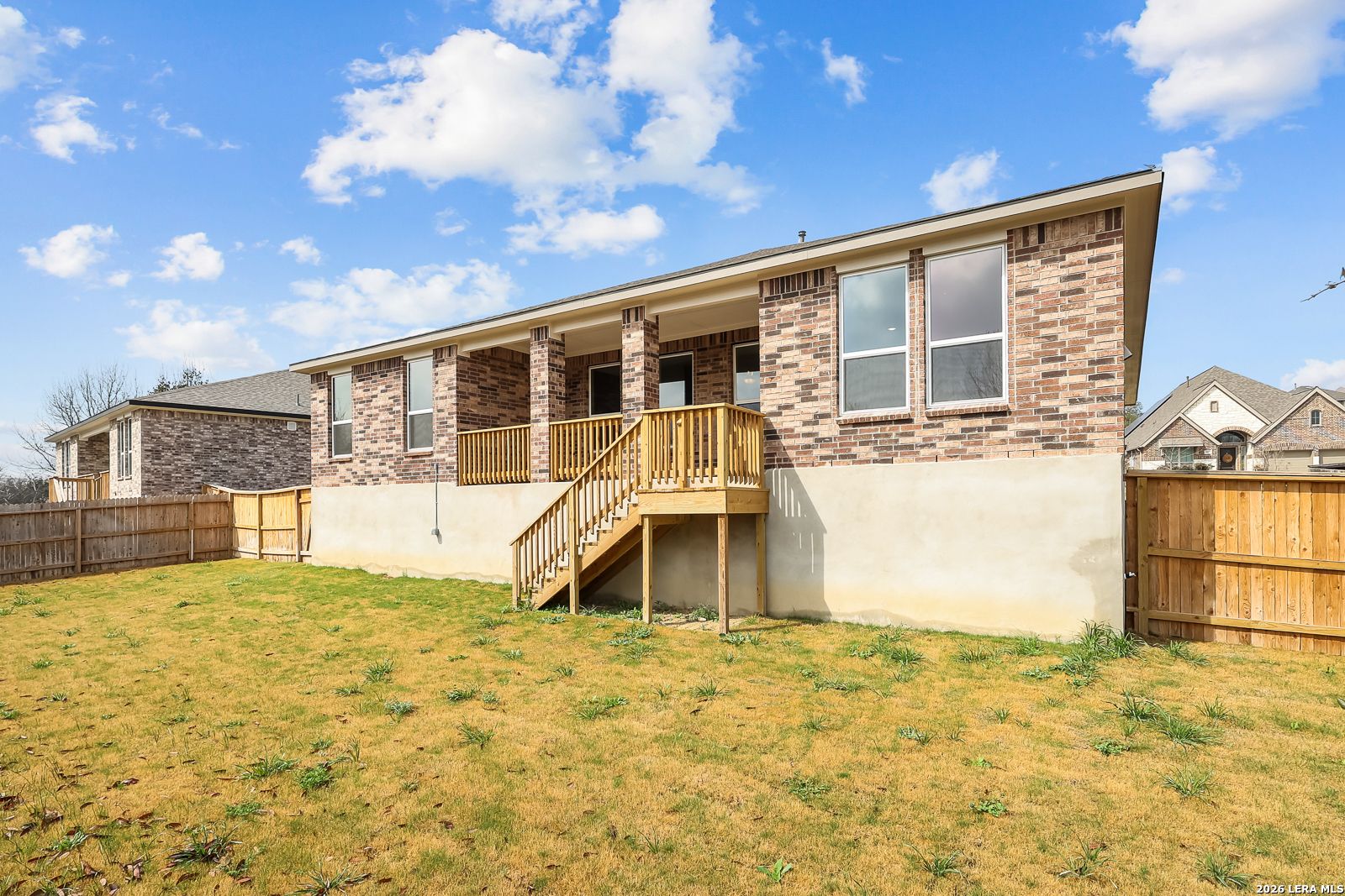 Single-story brick home with covered porch, wooden deck stairs, and fenced grassy yard in Ladera, San Antonio: Davidson Homes The Rockford G