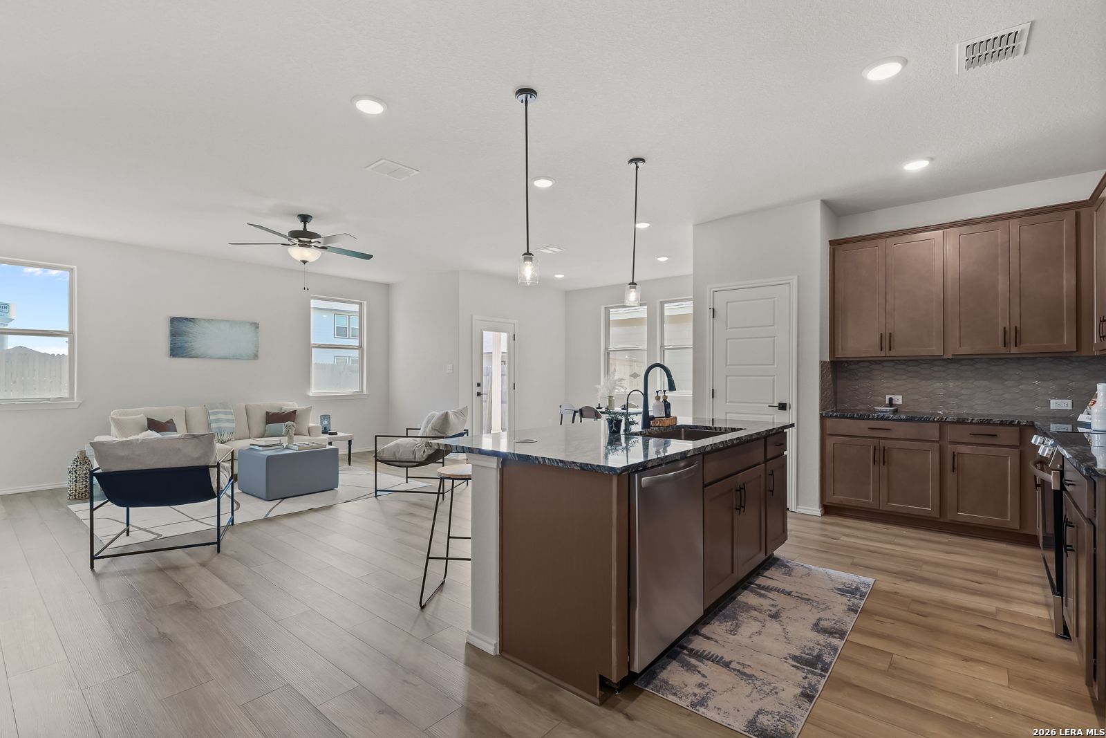 Open-concept living and kitchen with large island, granite counters, stainless appliances, and cozy seating in The Daphne H, Seguin, Texas