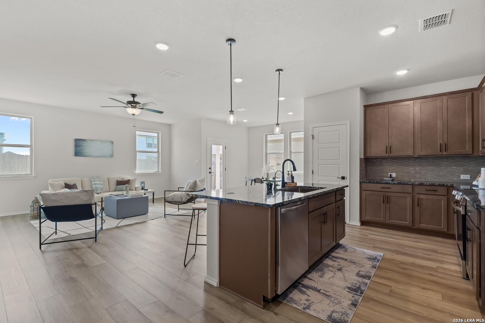 Open-concept living and kitchen with large island, granite counters, stainless appliances, and cozy seating in The Daphne H, Seguin, Texas