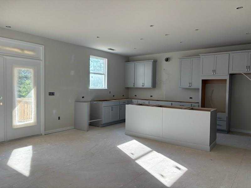 Modern unfinished kitchen with gray cabinets, large white island, and balcony views in Davidson Homes The Hickory A, Riverwood, Dallas, GA