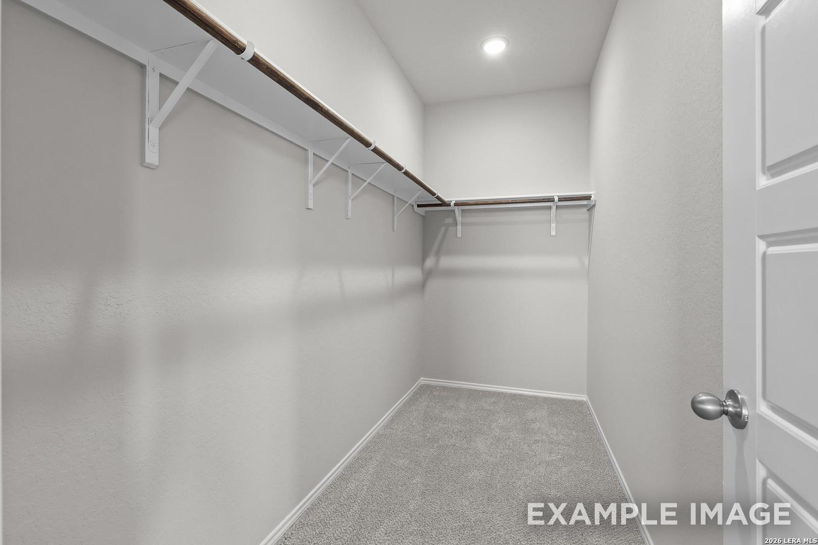 Spacious walk-in closet with wooden shelves, hanging rods, gray carpet in Davidson Homes The Colorado B, Agave, San Antonio