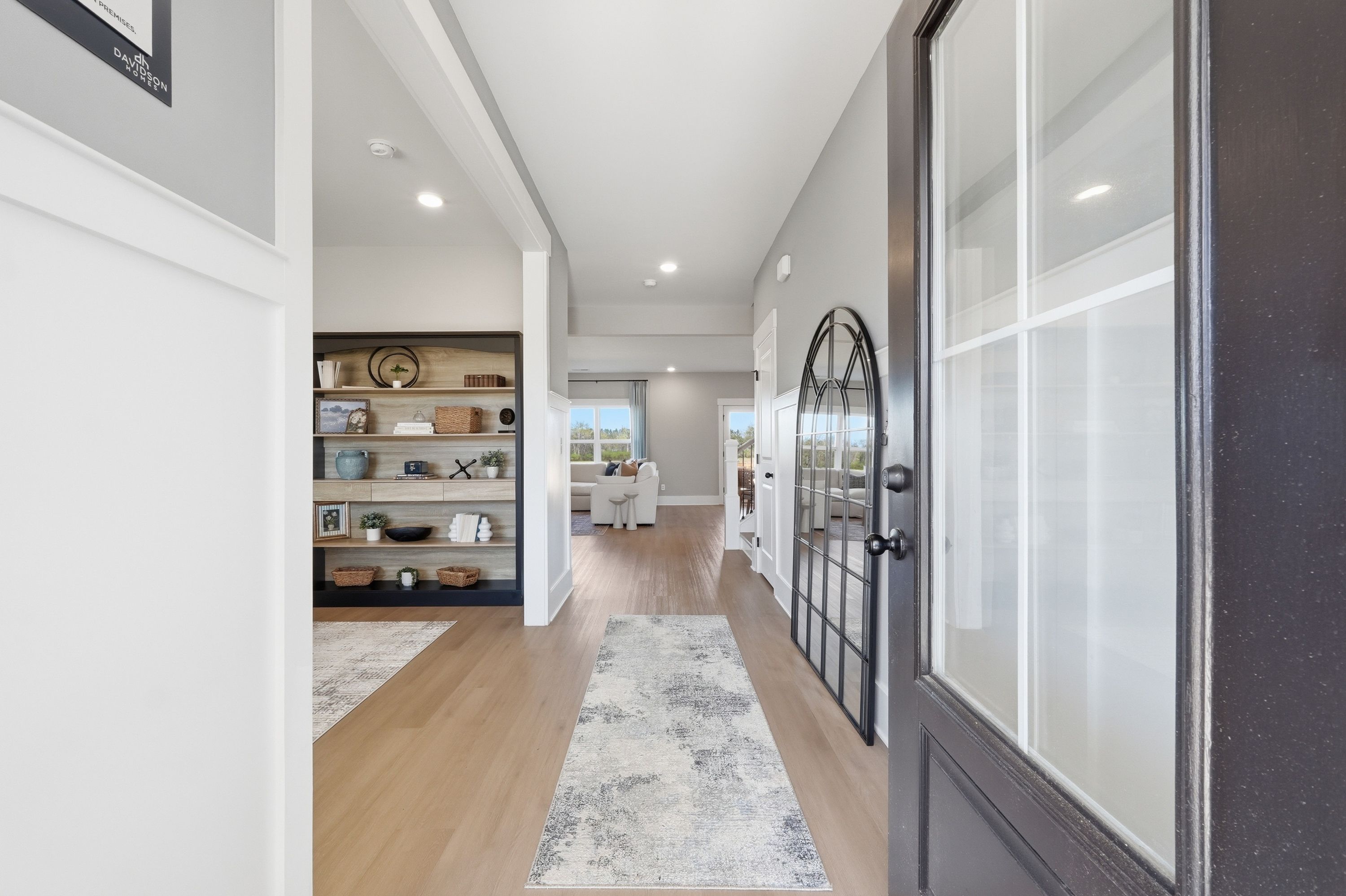 Spacious foyer with arched glass front door, hardwood floors, gray runner rug, and built-in bookshelves at Berry Cove in New Market, Alabama