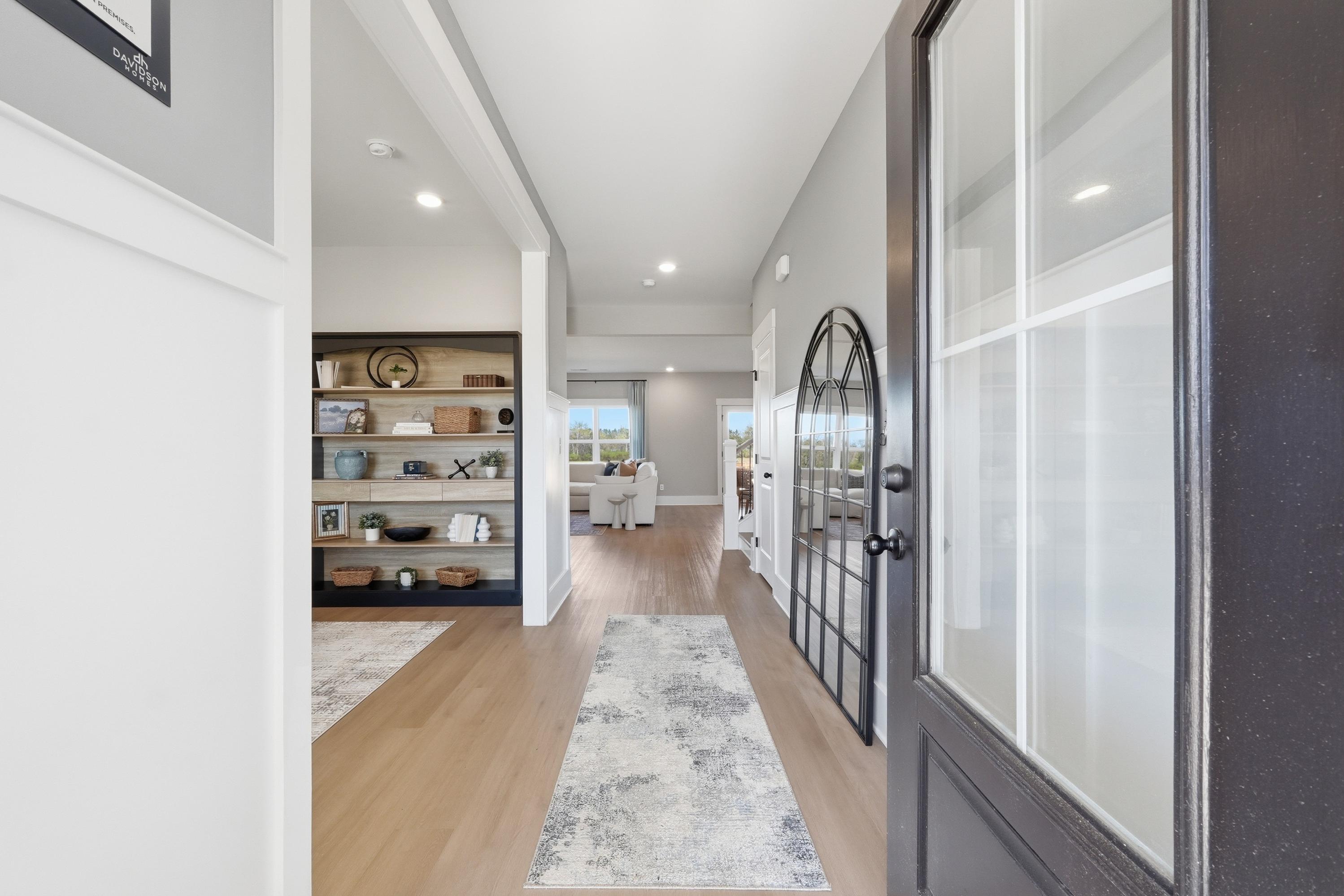Spacious foyer with arched glass front door, hardwood floors, gray runner rug, and built-in bookshelves at Berry Cove in New Market, Alabama