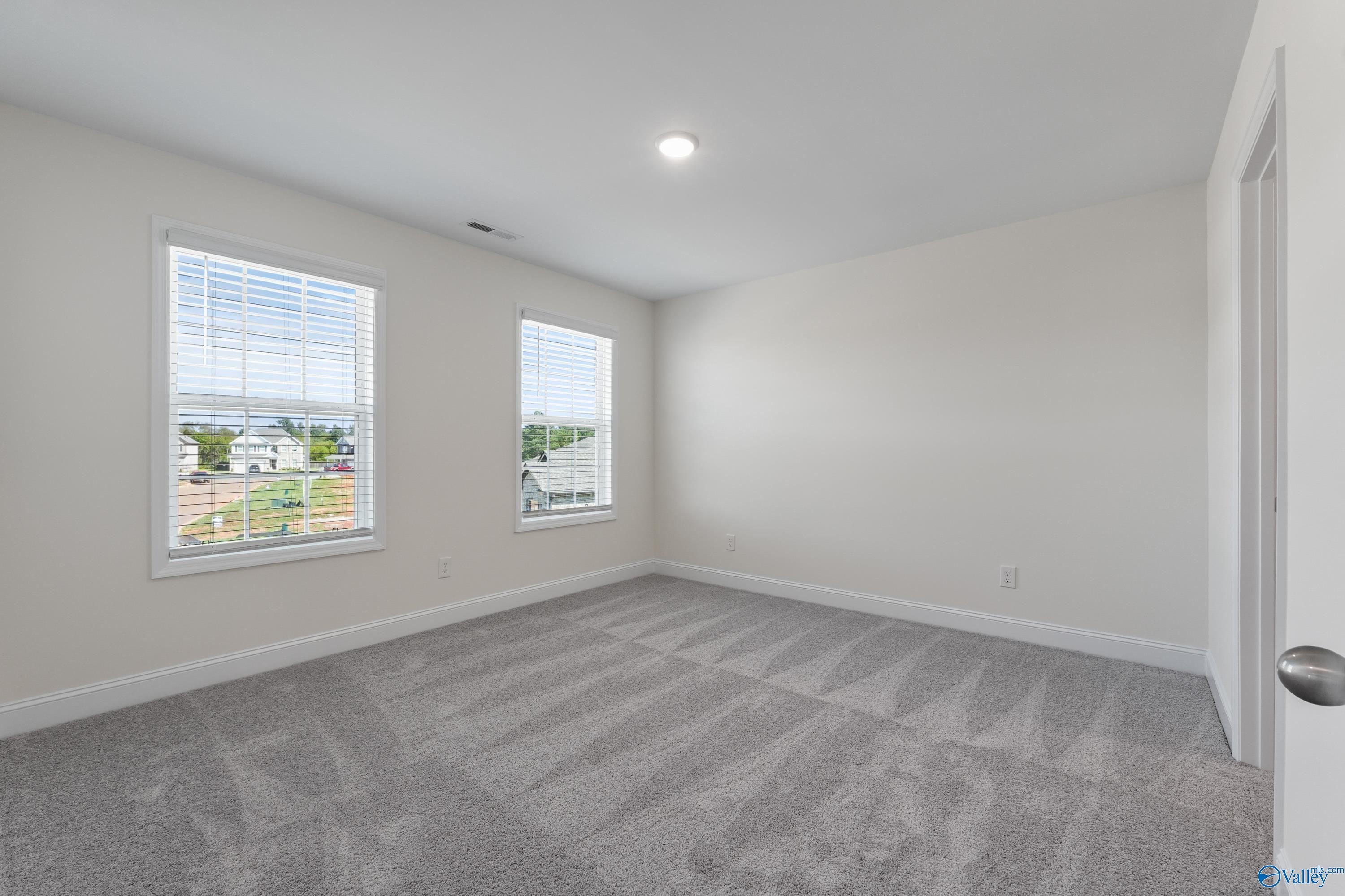 Bright empty bedroom with beige walls, dual large windows with blinds, gray carpet in Davidson Homes The Shelby A, Athens AL