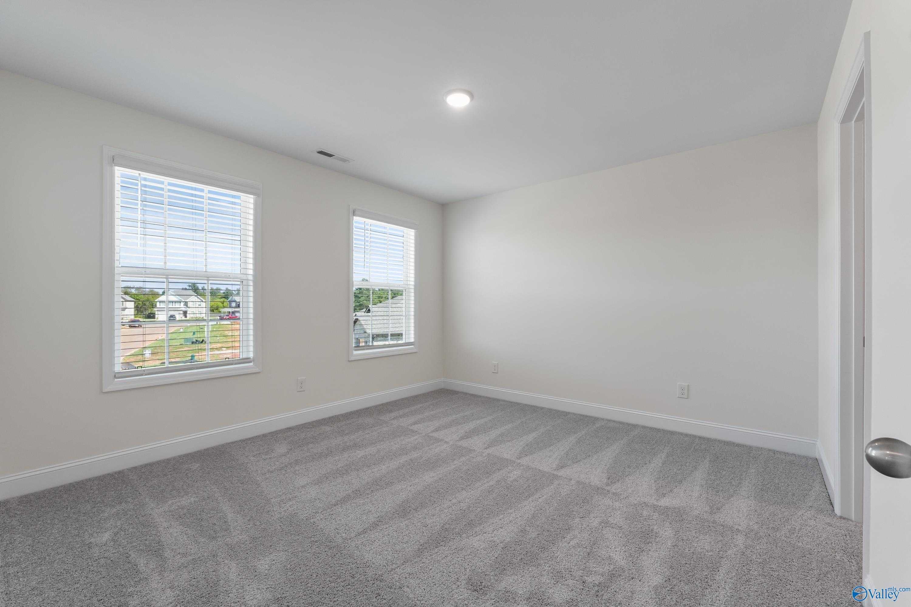 Bright secondary bedroom with beige walls, gray carpet, and neighborhood views in Davidson Homes The Shelby A, Athens, Alabama