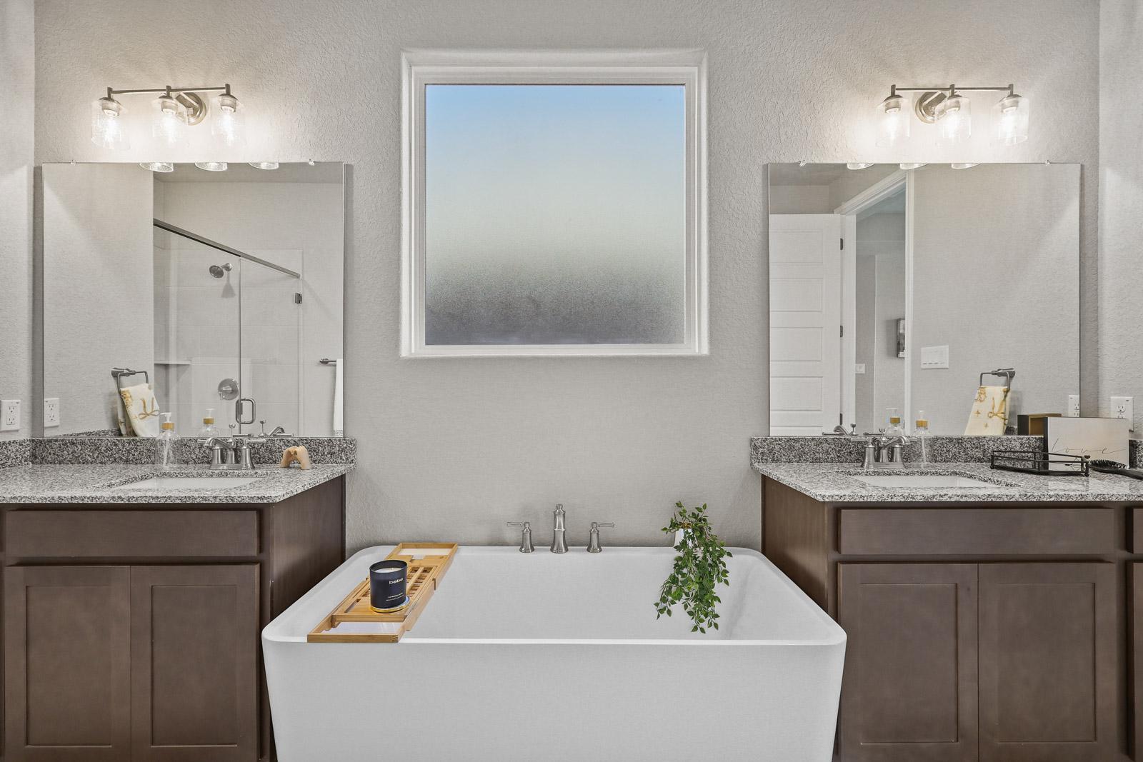 Modern master bathroom in The Jennings G featuring a soaking tub, dual granite vanities, and bright natural light.