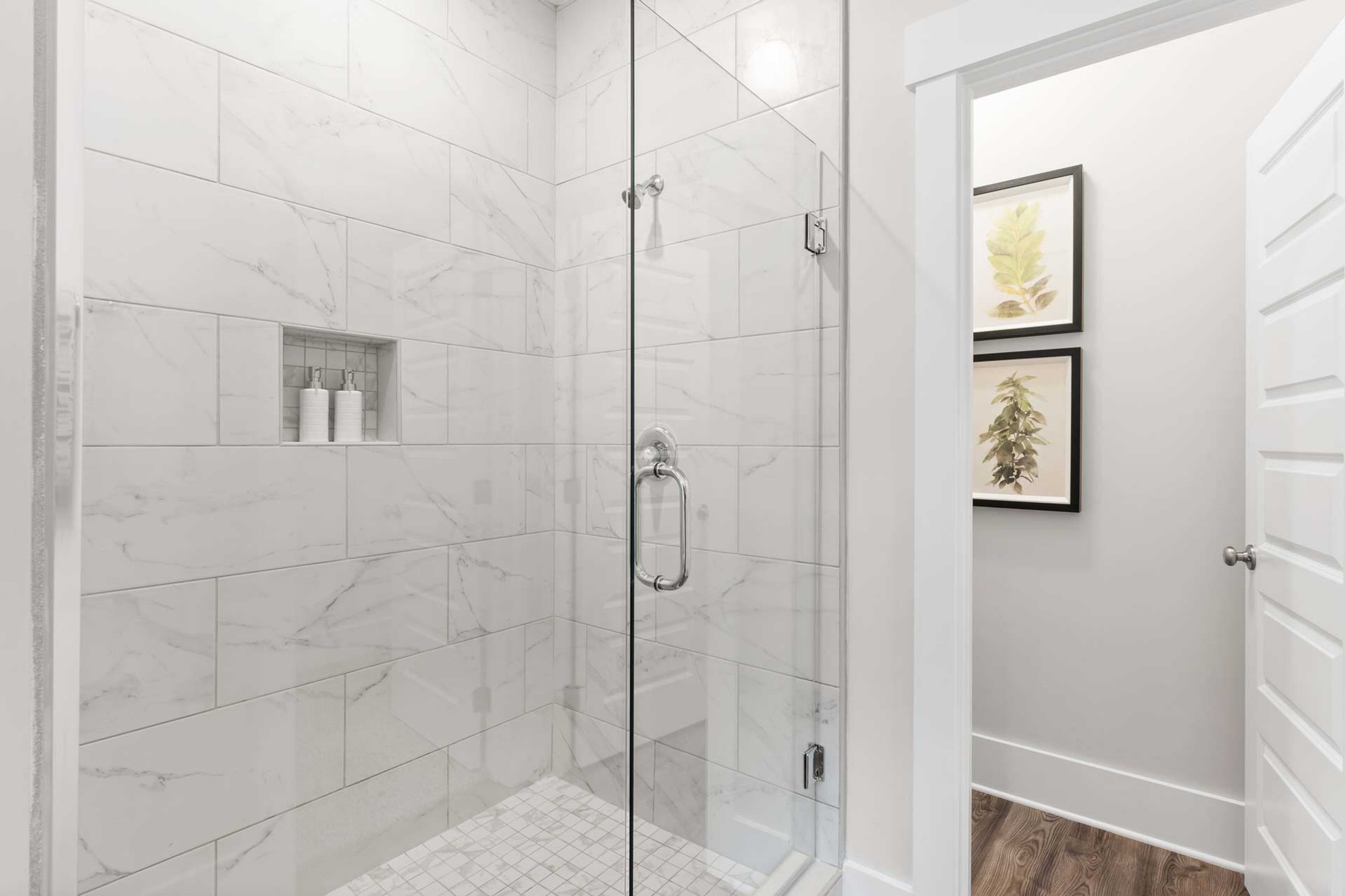 Spacious white subway tile shower with frameless glass door and niche shelf at The Meadows in Athens, Alabama