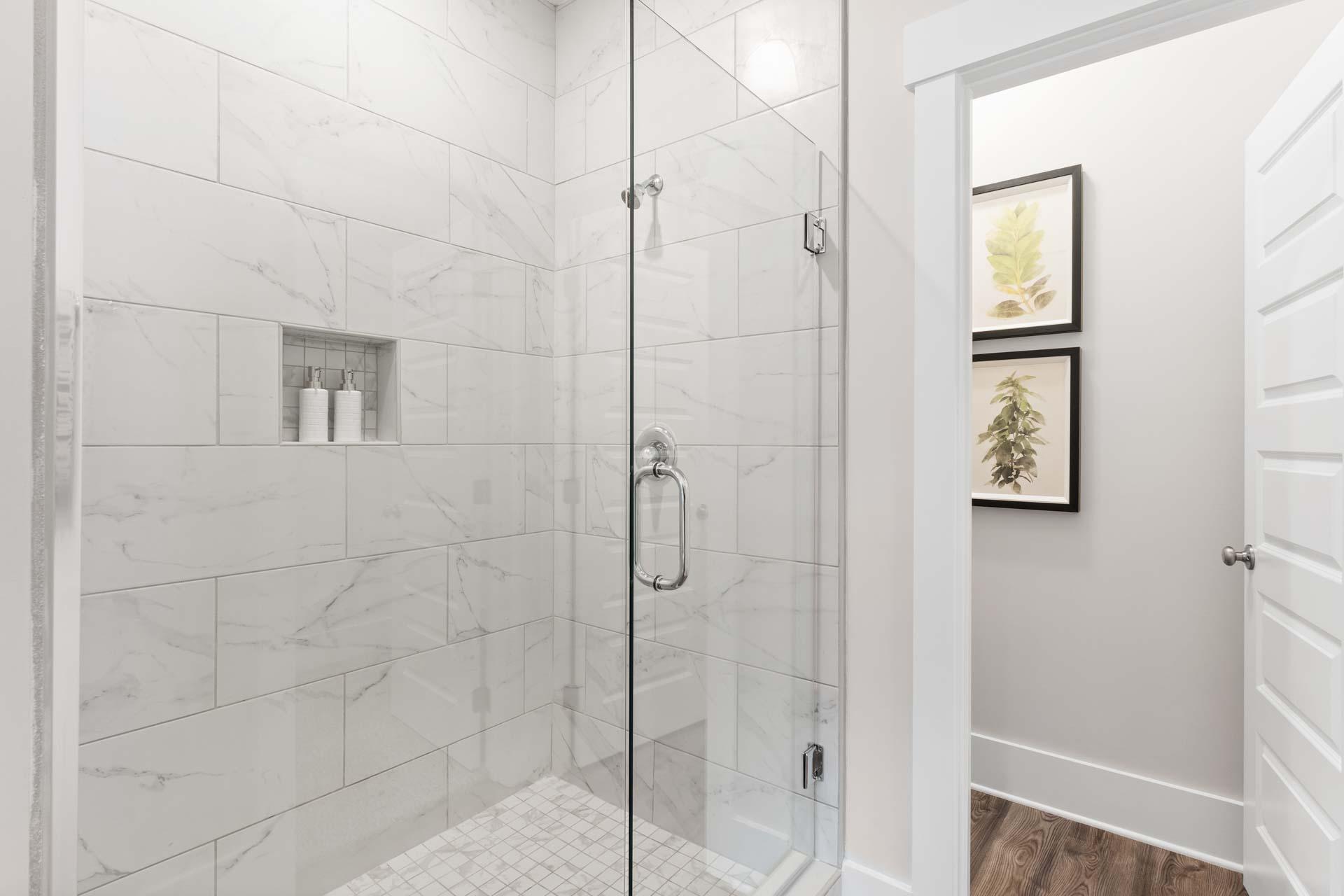 Spacious white subway tile shower with frameless glass door and niche shelf at The Meadows in Athens, Alabama