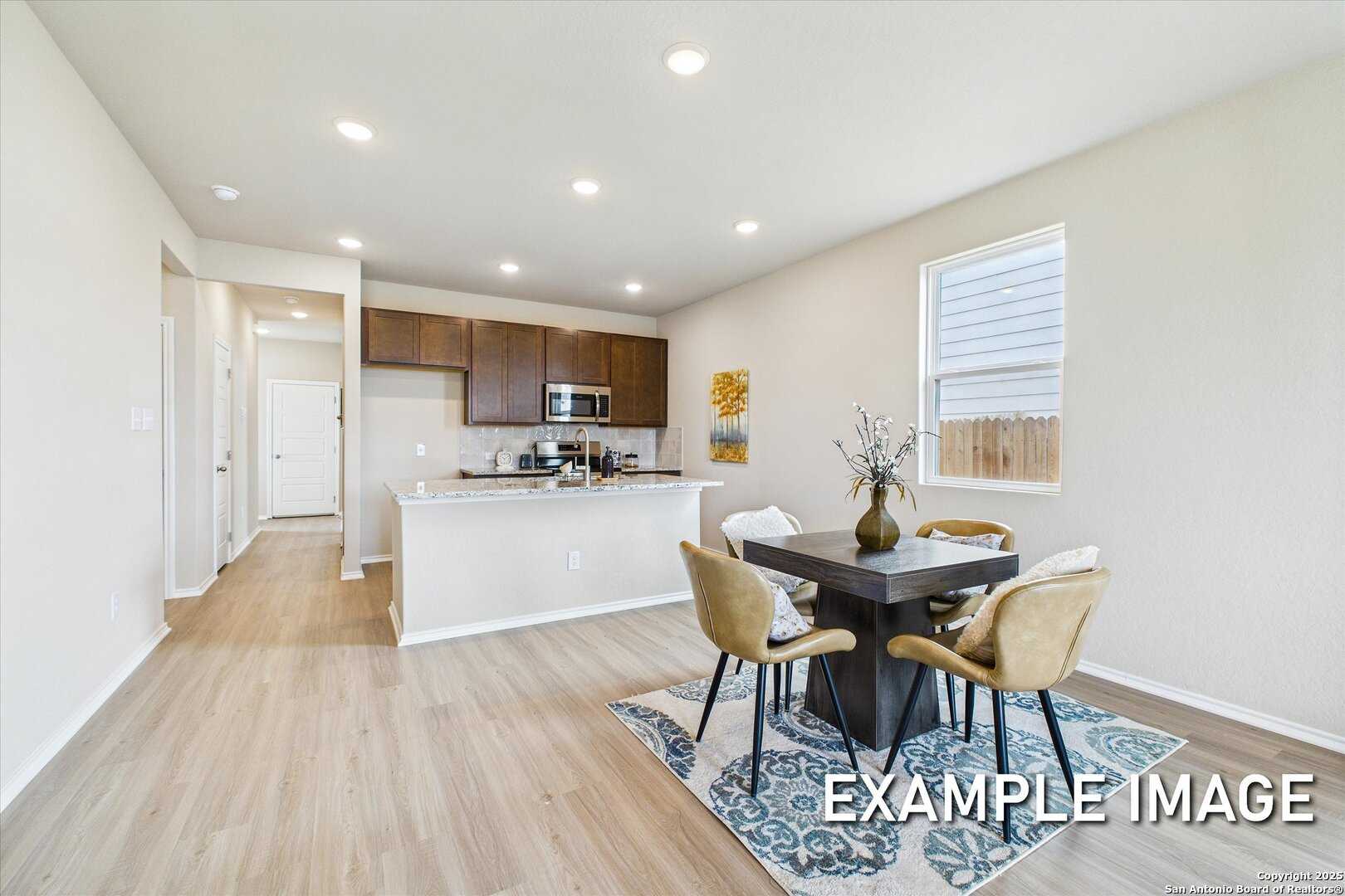 Modern open-concept kitchen and dining area with white cabinets, dark wood table, and hardwood floors in Davidson Homes The Comal B, San Antonio
