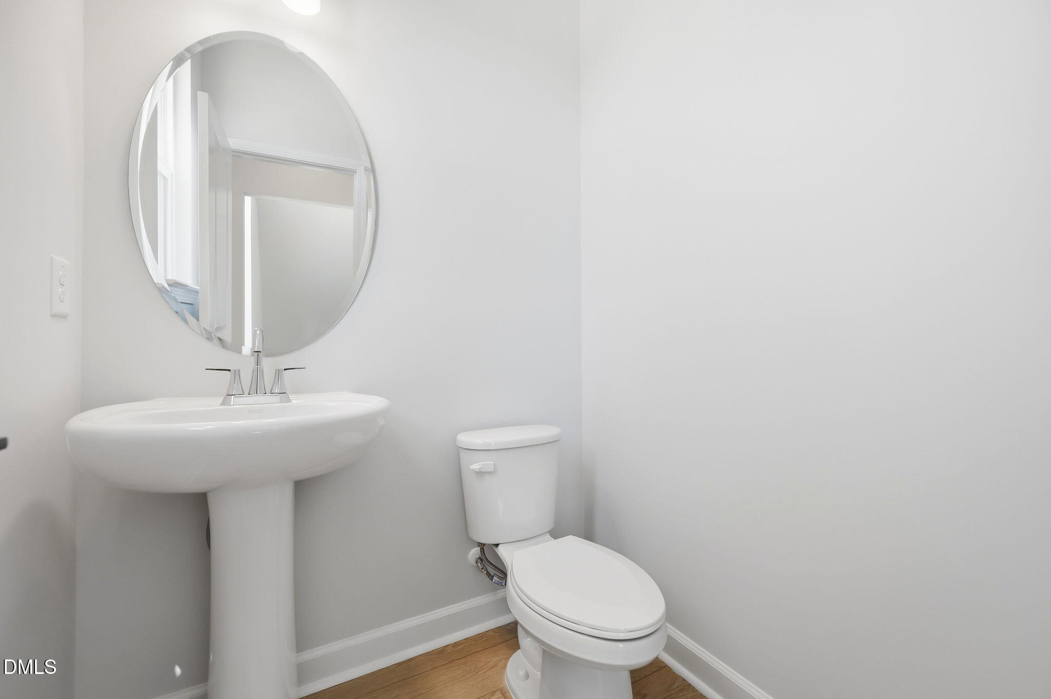 Modern powder room with pedestal sink, oval mirror, and hardwood floors in The Avery home, Forestville Yard, Knightdale, NC.